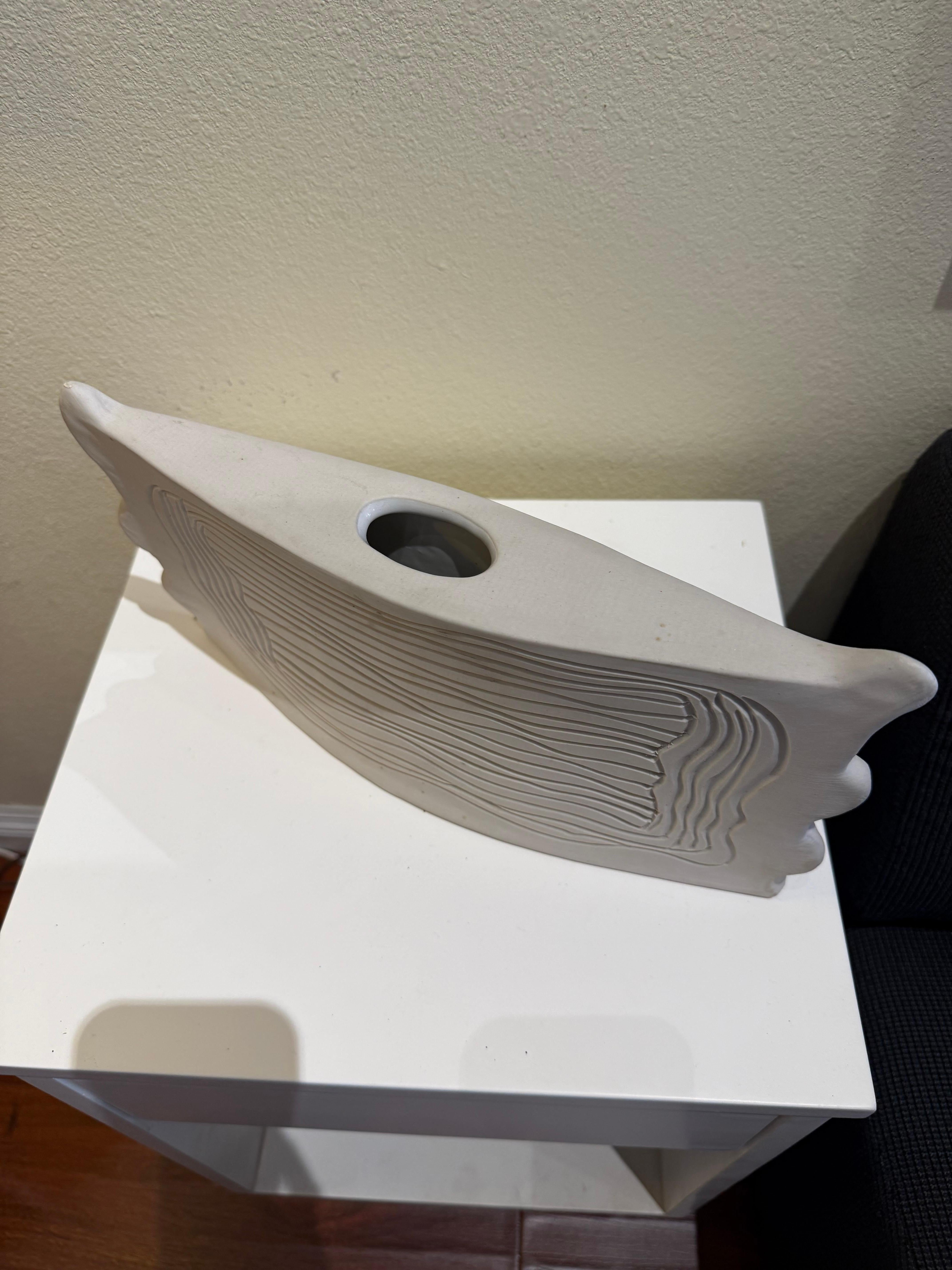 Questo vaso in ceramica realizzato a mano da Dora De Larios esemplifica il suo approccio raffinato alla forma e alla superficie. L'imbarcazione si allontana dalla tradizionale simmetria cilindrica, adottando invece una silhouette scultorea con bordi