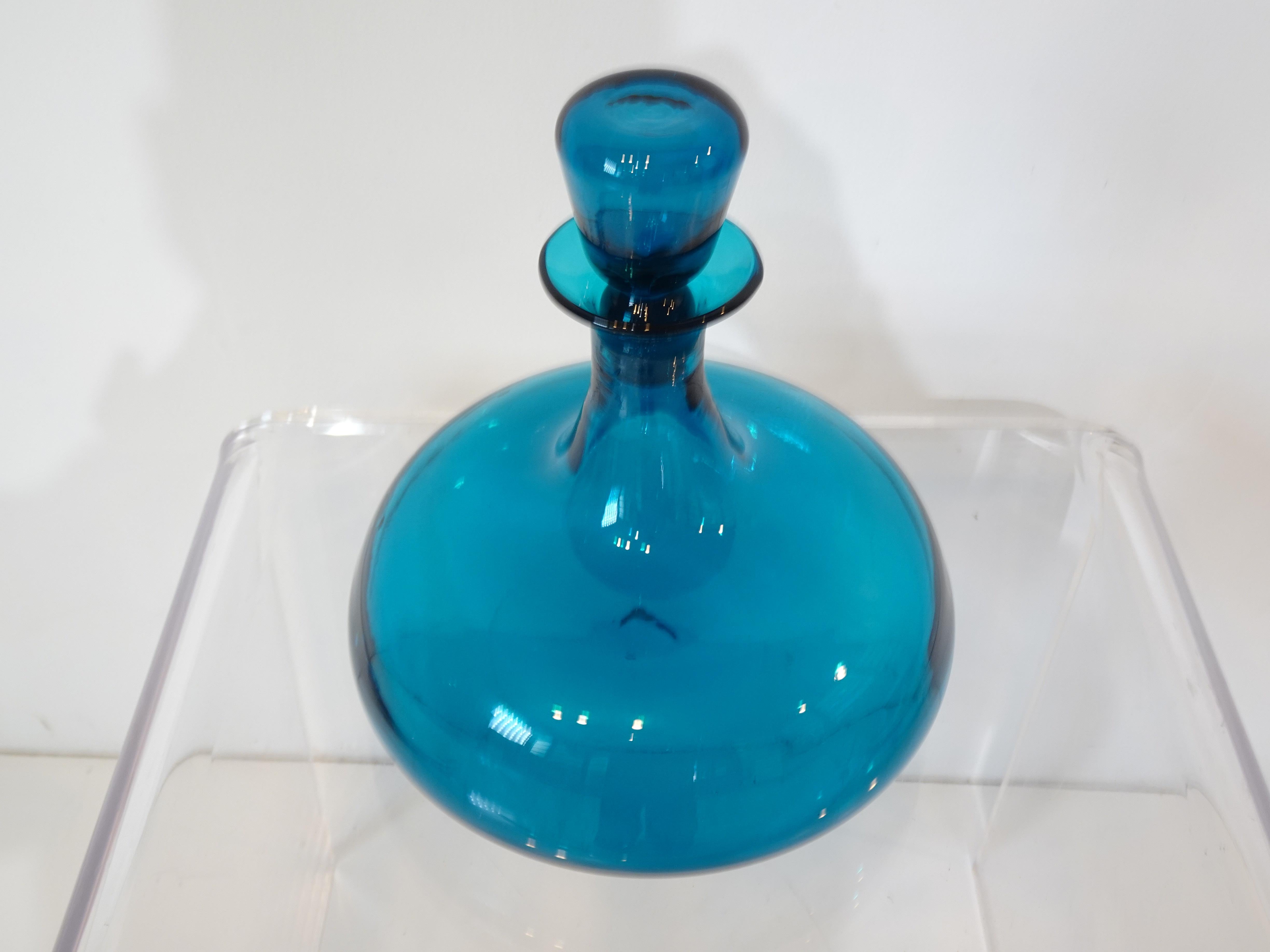 A nice handblown blue glass decanter with matching stopper designed and executed by well regarded glassblower Wayne Husted for the Blenko Glass Company. These iconic pieces were the statement accessory for Mid Century interiors and are as fresh