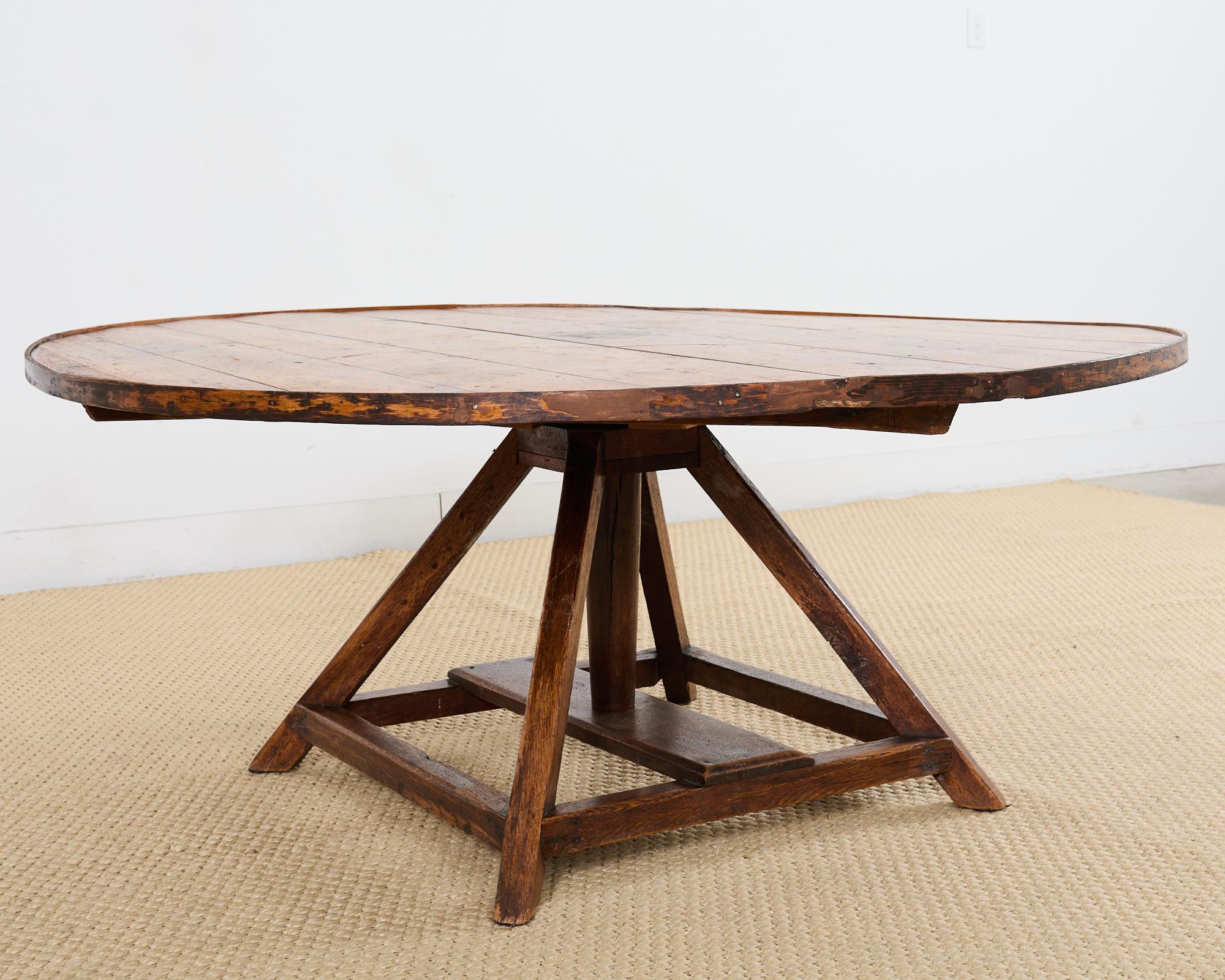 Rustic country Italian round farmhouse dining table or games table featuring a trestle style pedestal base. The table has a large round plank top crafted from pine with an aged, weathered and distressed patina. The round table top turns like a lazy