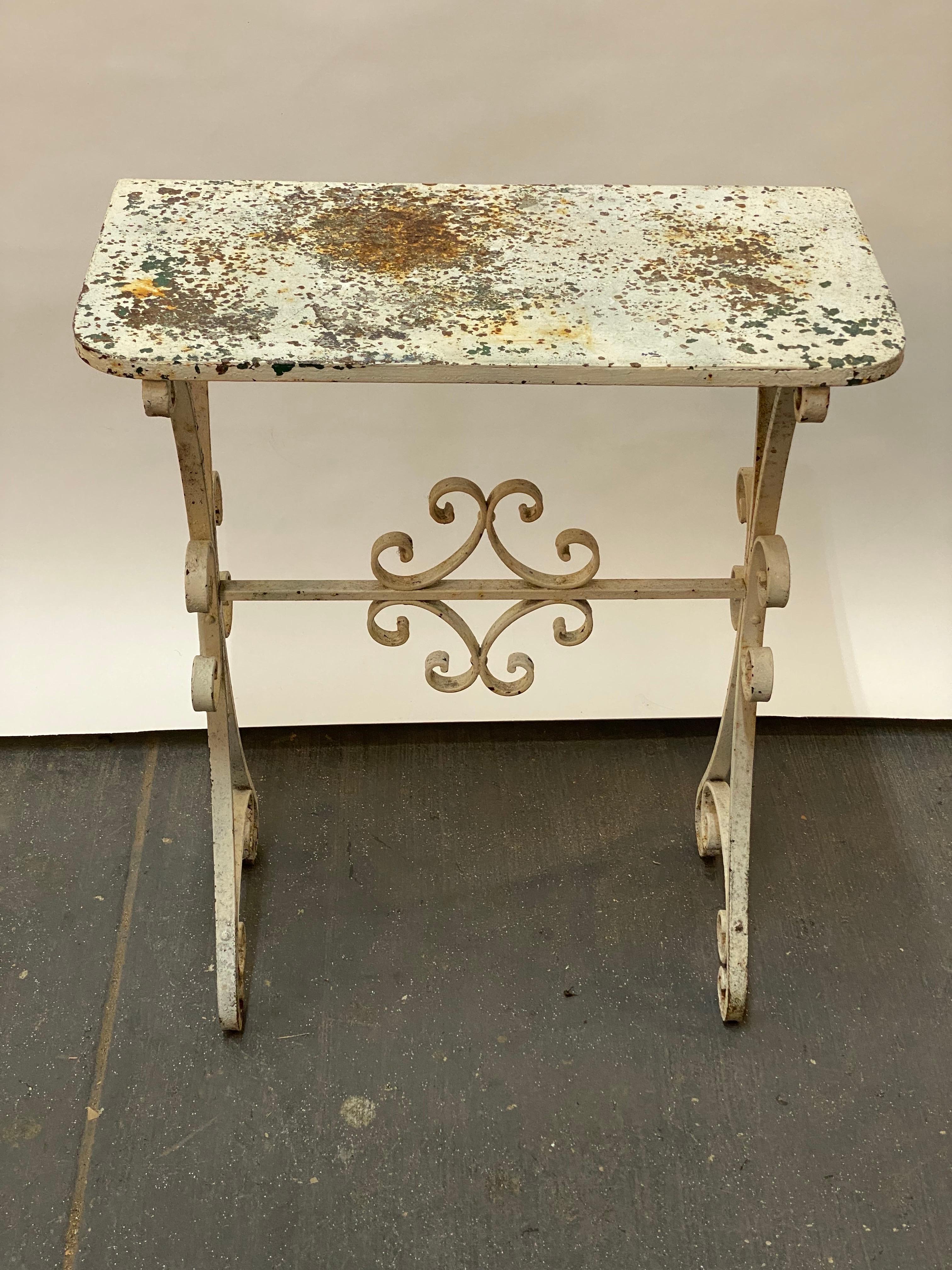 A nicely detailed weathered wrought iron console table. The piece displays several coats of aged and weathered paint, which adds to the piece's charm; white on top of a dark forest green. The stretcher base is scrolled with two stars on each end.
