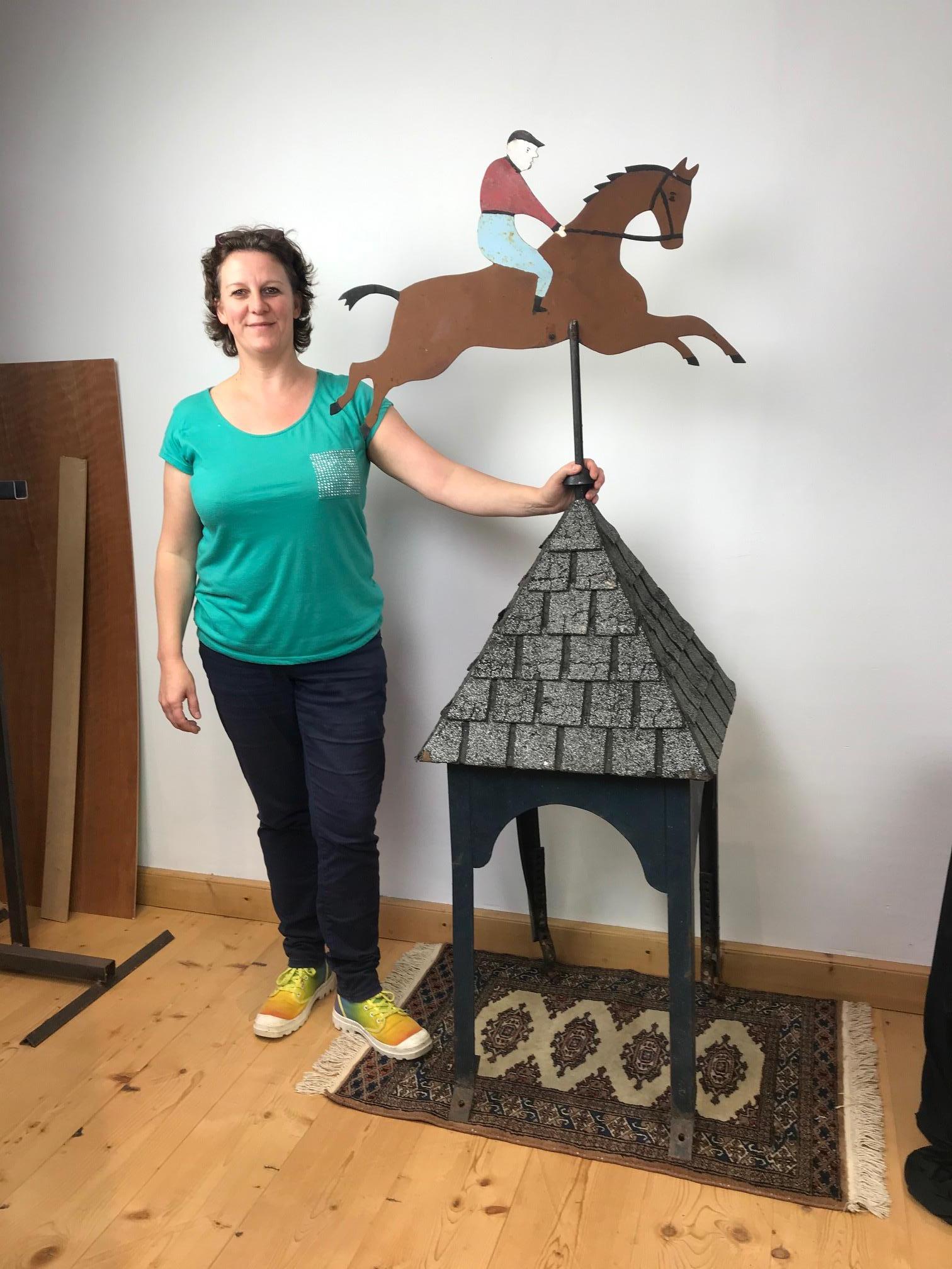 Vintage pointed roof with a weathervane in the shape of a horse with jockey rider. 
This jockey riding race horse is made from cut metal, is hand painted and double sided. 
This wind vane roof ornament is mounted on a pointed roof which is covered