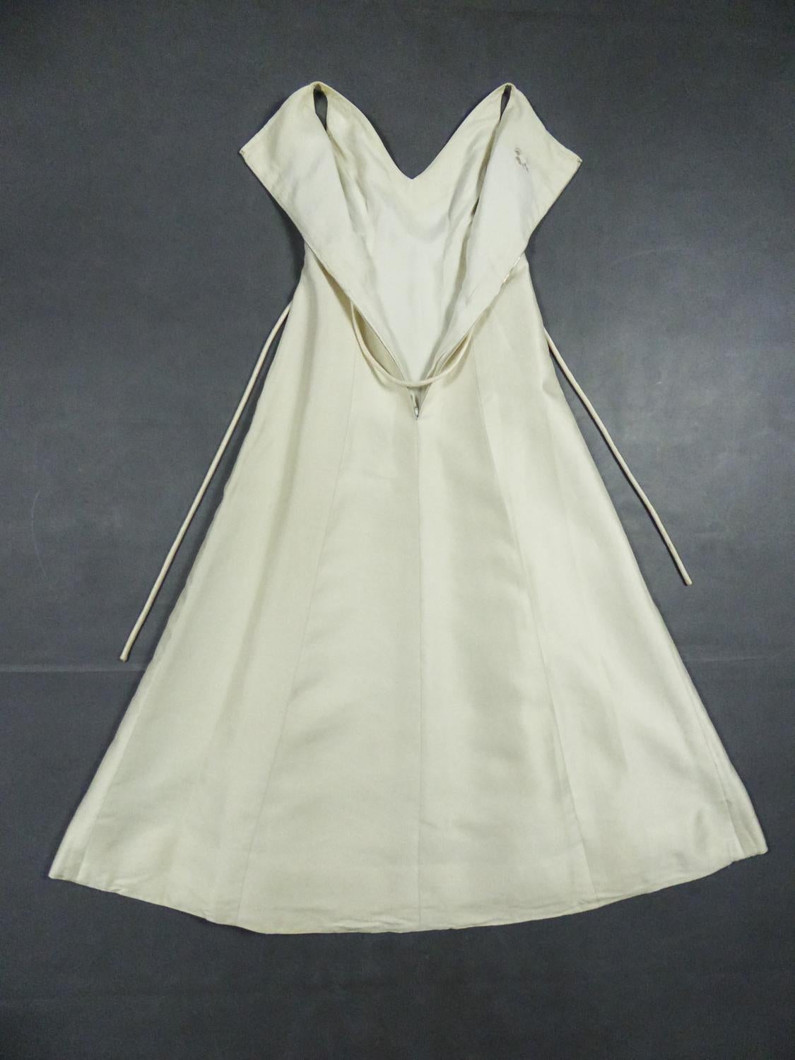 Circa 1965
British Colony of Hong Kong

Elegant wedding dress in off-white rigid silk gazar from the 1960s. Long dress with high waist fitted on the bust and sleeveless. V-shaped neckline and large box pleats at the front to give full sweep to the