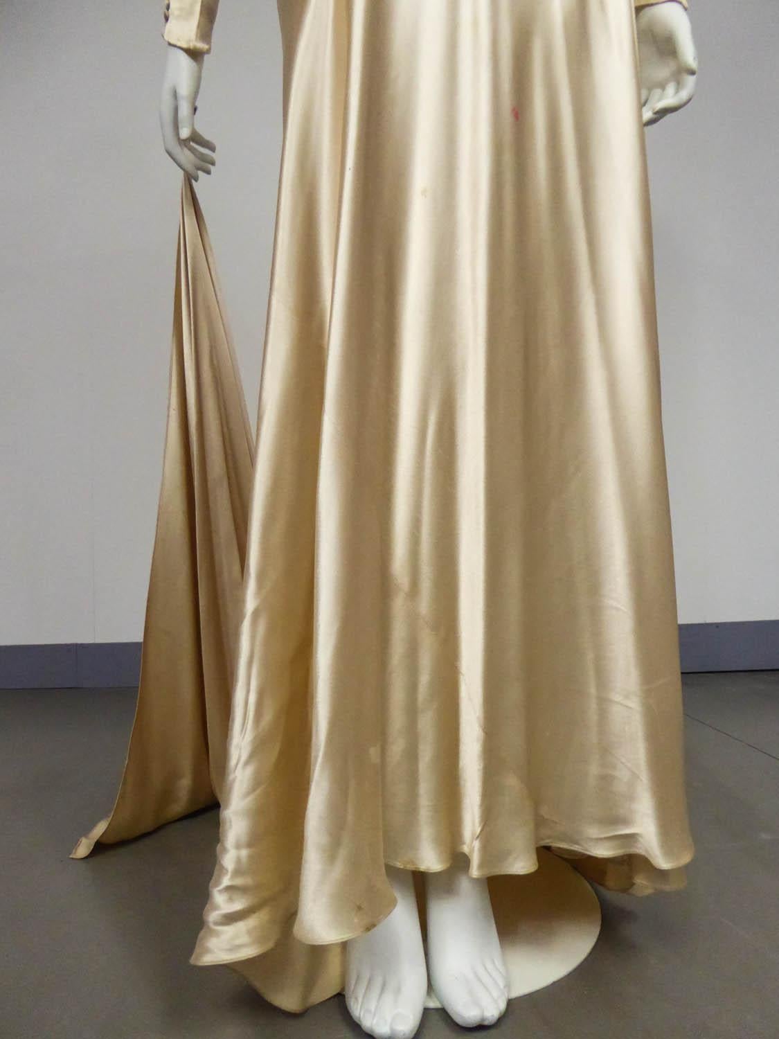 Circa 1935/1945
France

Wedding dress in champagne silk satin from the late 1930s. Fluid and skin-tight cut in bias with a pleated work on the chest highlighting a sheath silhouette. Long sleeves adorned with a long row of matching buttons and