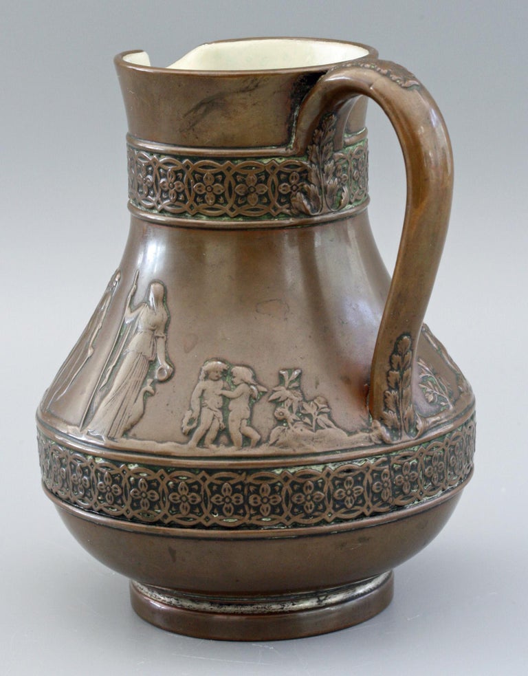 A rare Wedgwood copper dipped jasperware jug with classical figures dating from the early to mid-19th century. The ceramic jug has a copper coating over a molded base with typical classical figures in relief around the body and set between raised