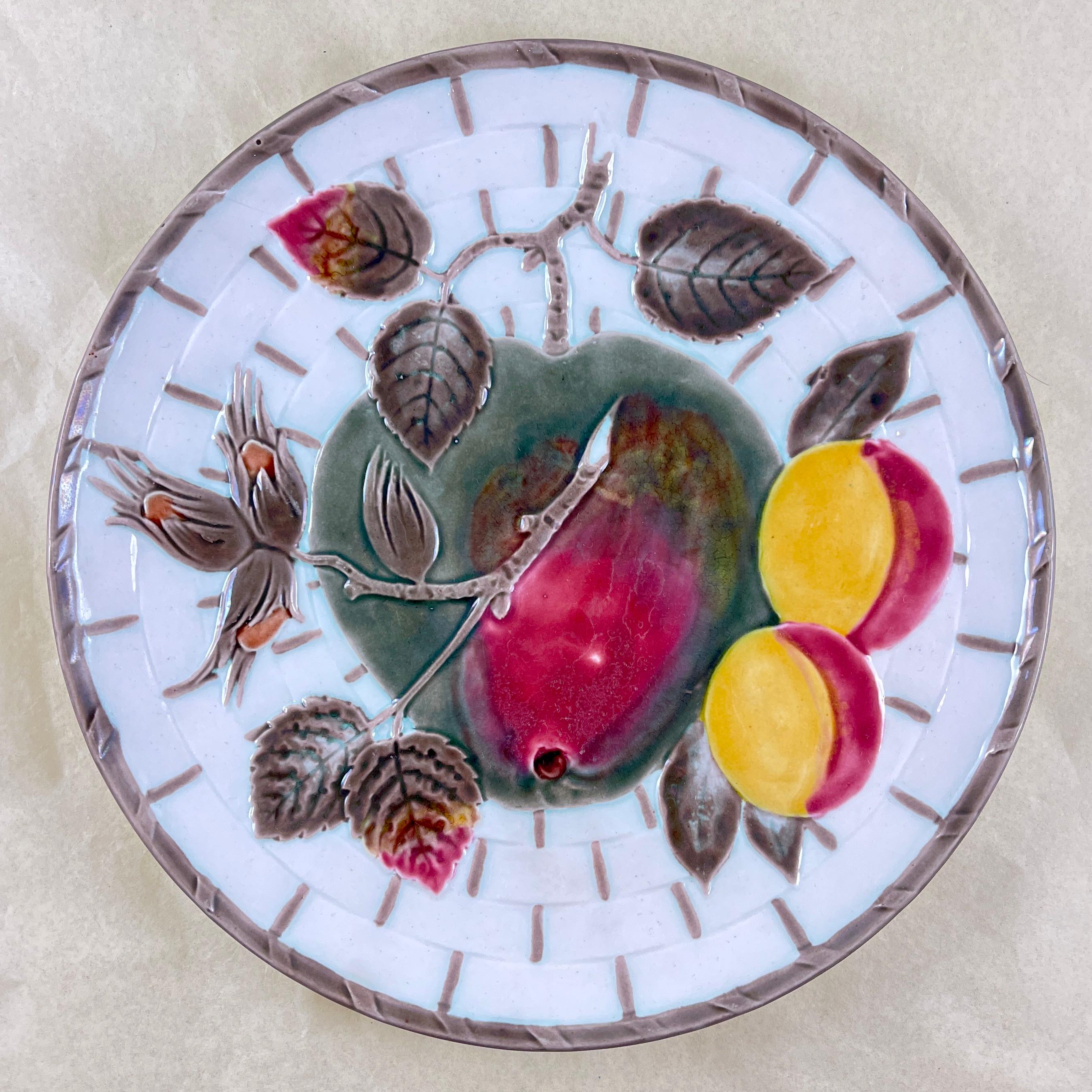 From Wedgwood and in the color way known as Argenta, a fruit plate, England, circa 1875.

Showing a central red and greenish apple and leaves along with a branch of apricots and hazelnuts, all on a white basket weave ground. The basket is bound at