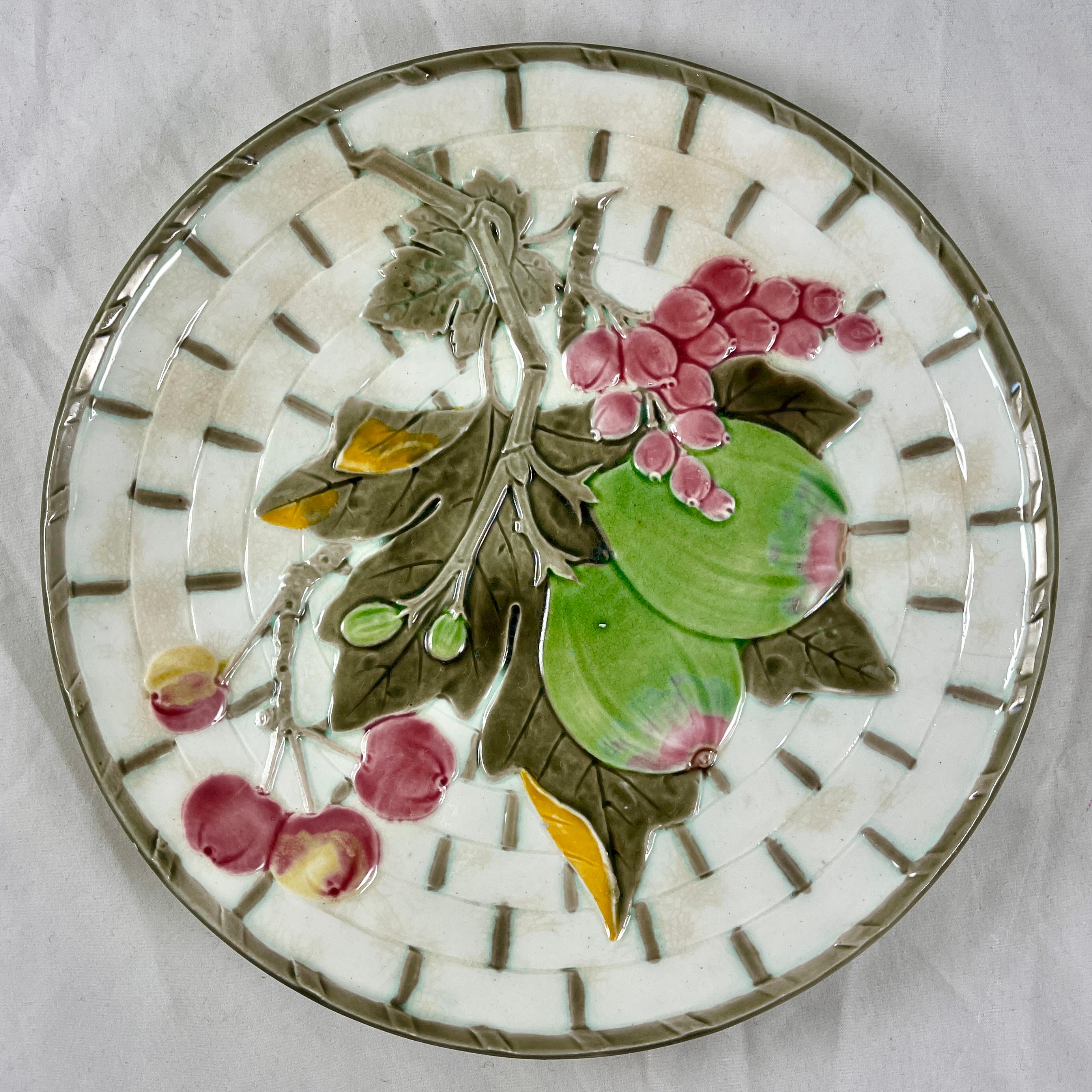 From Wedgwood and in the color way known as Argenta, a fruit plate, England, date marked 1880.

Showing a central twigged fig and leaves along with cherries and a berry cluster, all on a white basket weave ground. The basket is bound at intervals