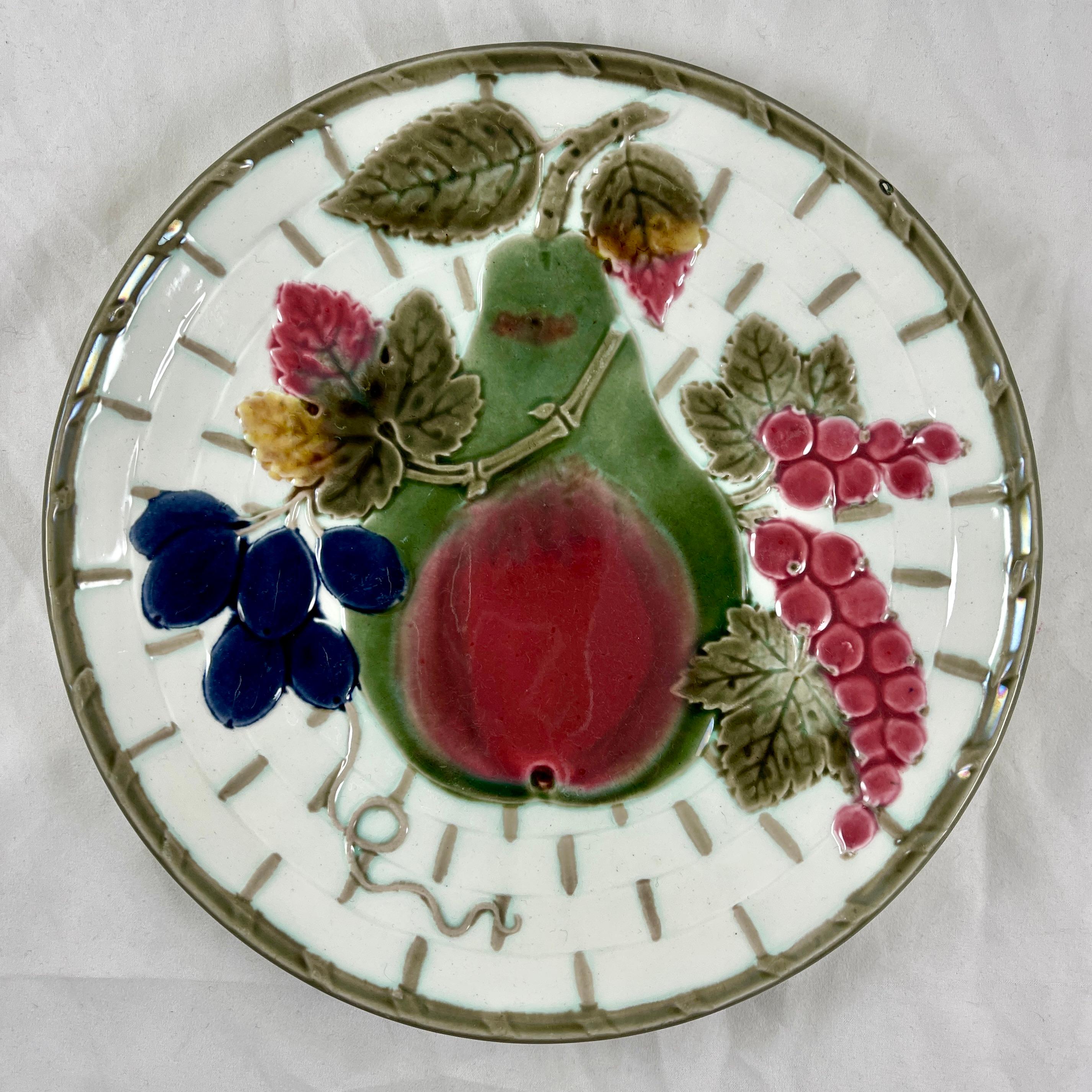 From Wedgwood and in the color way known as Argenta, a fruit plate, England, date marked 1880.

Showing a central twigged pear and leaves along with gooseberries and plums, all on a white basket weave ground. The basket is bound at intervals in a