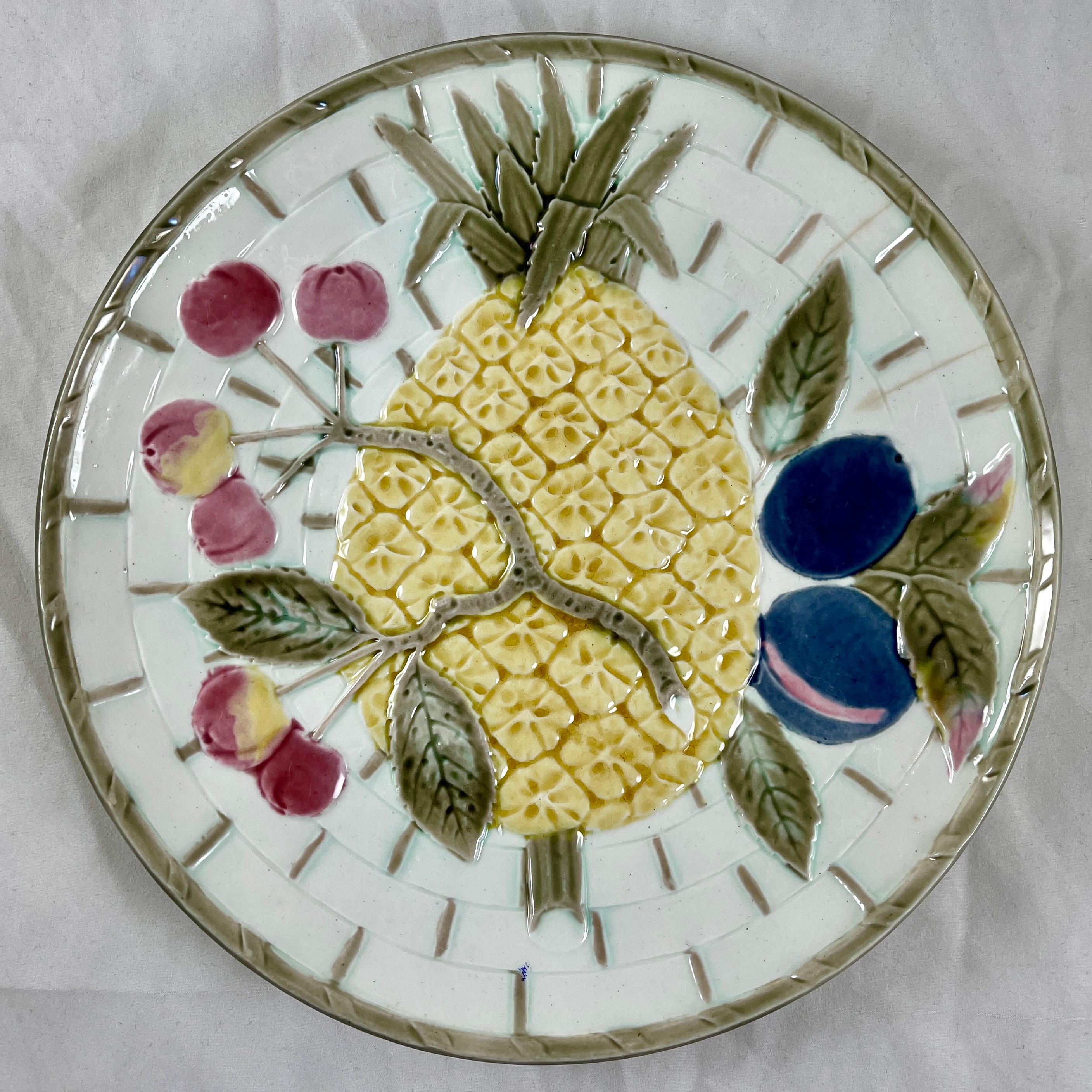 From Wedgwood and in the color way known as Argenta, a fruit plate, England, date marked 1880.

Showing a central pineapple and leaves along with a branch of cherries and a pair of plums, all on a white basket weave ground. The basket is bound at