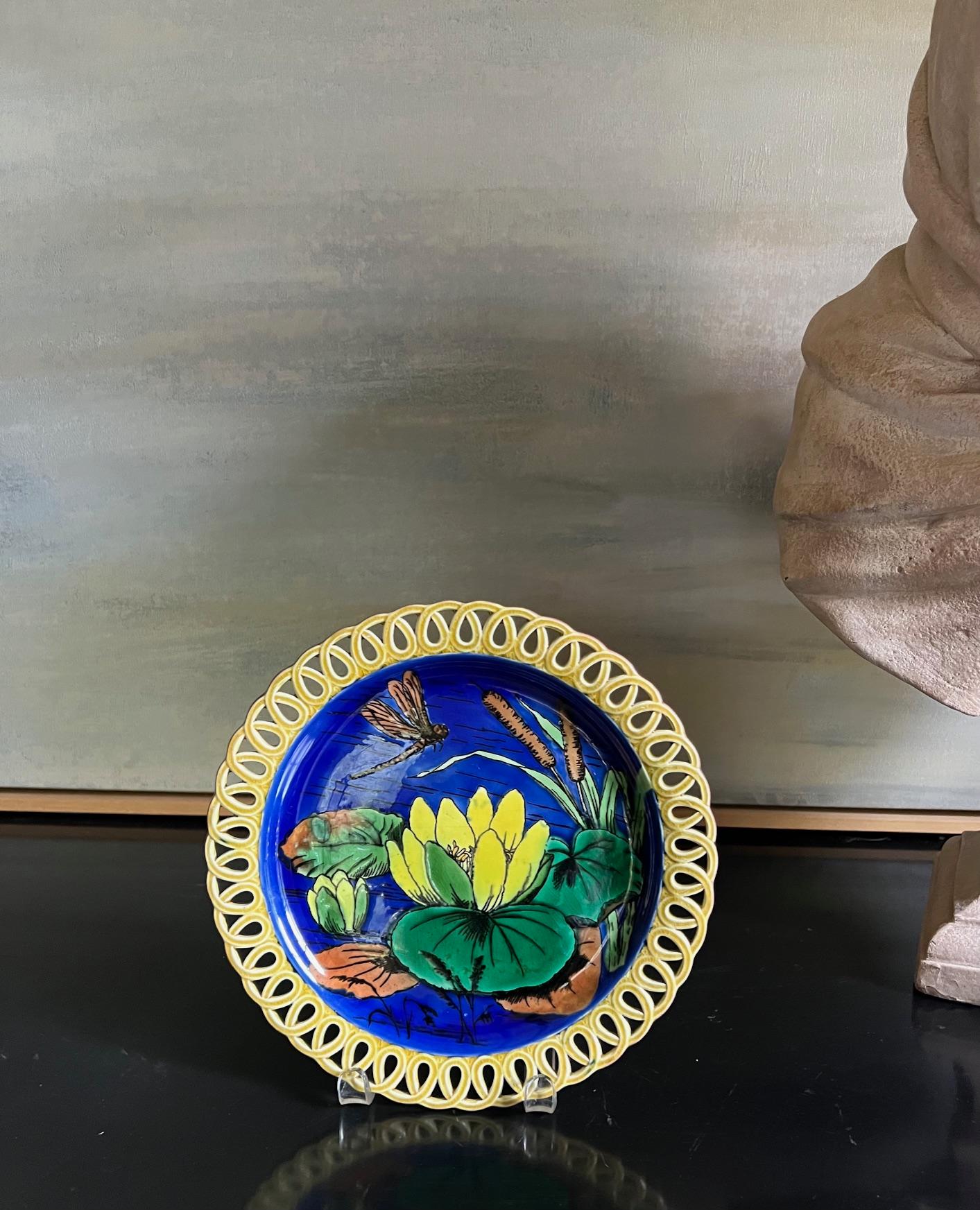 Assiette décorative en majolique du début de l'Art nouveau, fabriquée par Wedgwood en Angleterre en 1874. Les bords jaunes sont réticulés et le centre bleu cobalt est peint à la main avec un pad jaune et une libellule. Le dos porte l'empreinte de