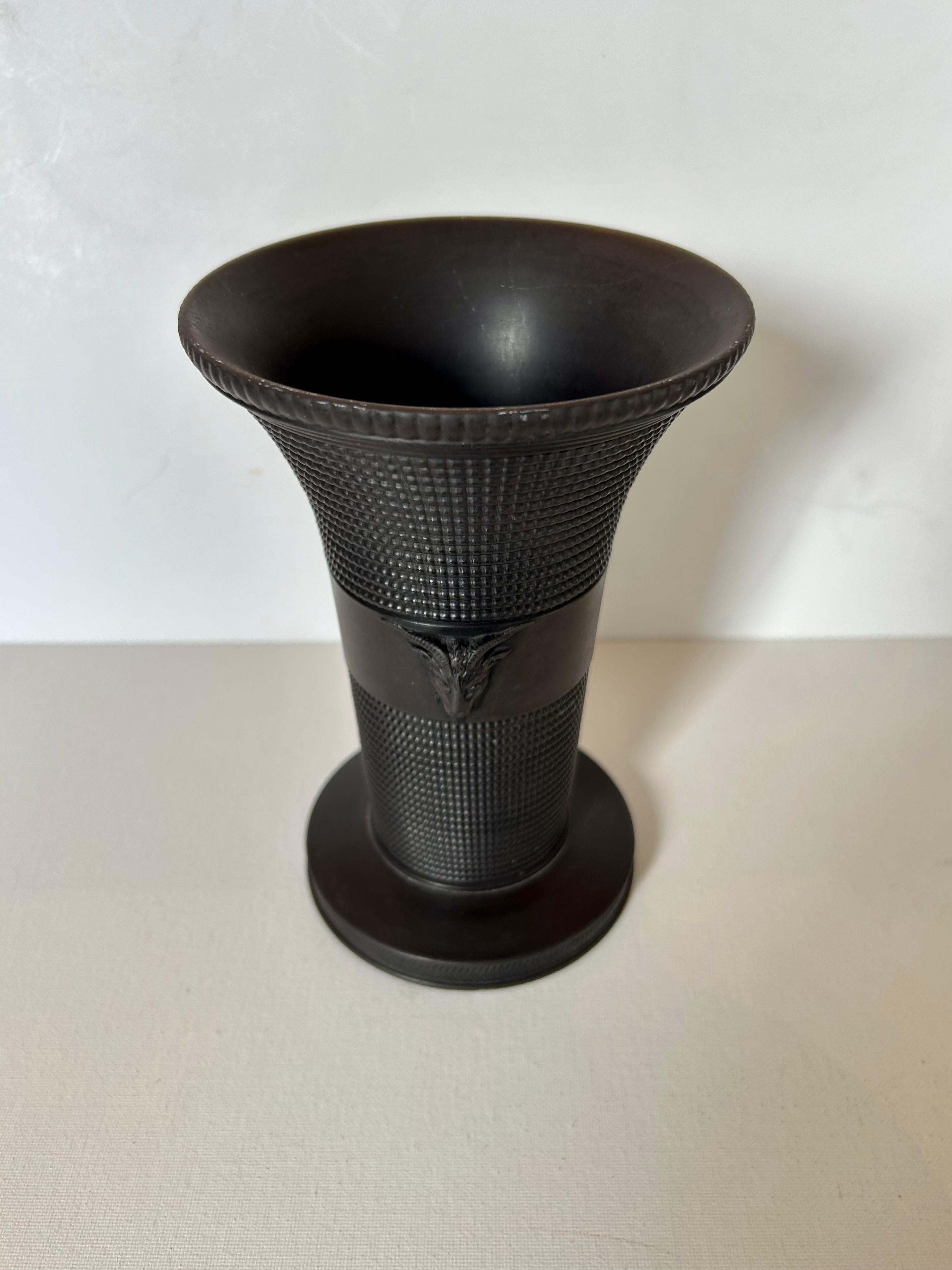 Si tratta di un vaso neoclassico in basalto di Wedgwood, del 1956 circa, dalla forma svasata, di colore nero opaco e con teste di ariete applicate su entrambi i lati. Marcato 