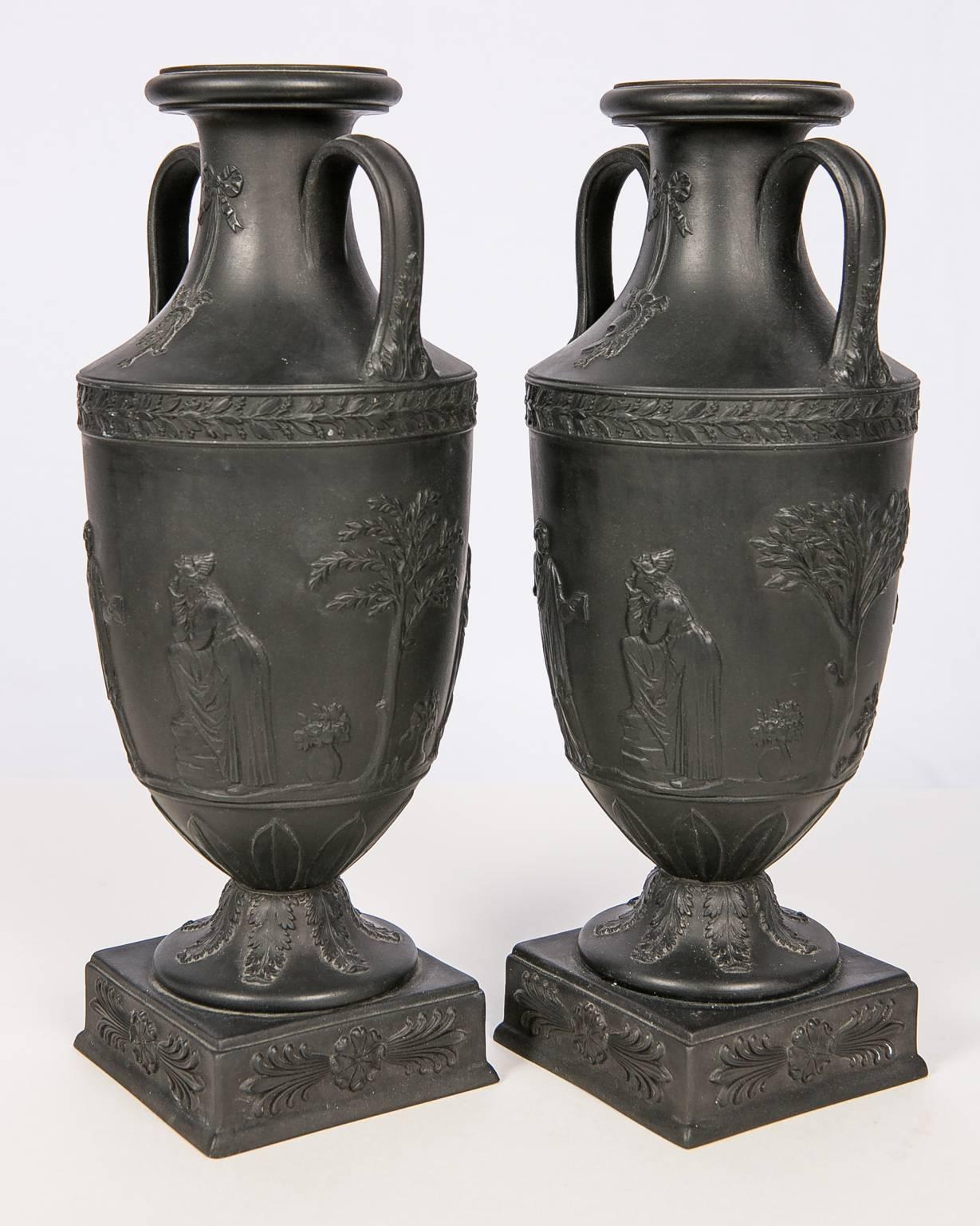 This pair of Wedgwood double handled mantel vases has a truly classical shape and decoration.
The expected Wedgwood molded design is finely executed. Around the center of the vases we see figures in relief wearing classical dress. Below the figures