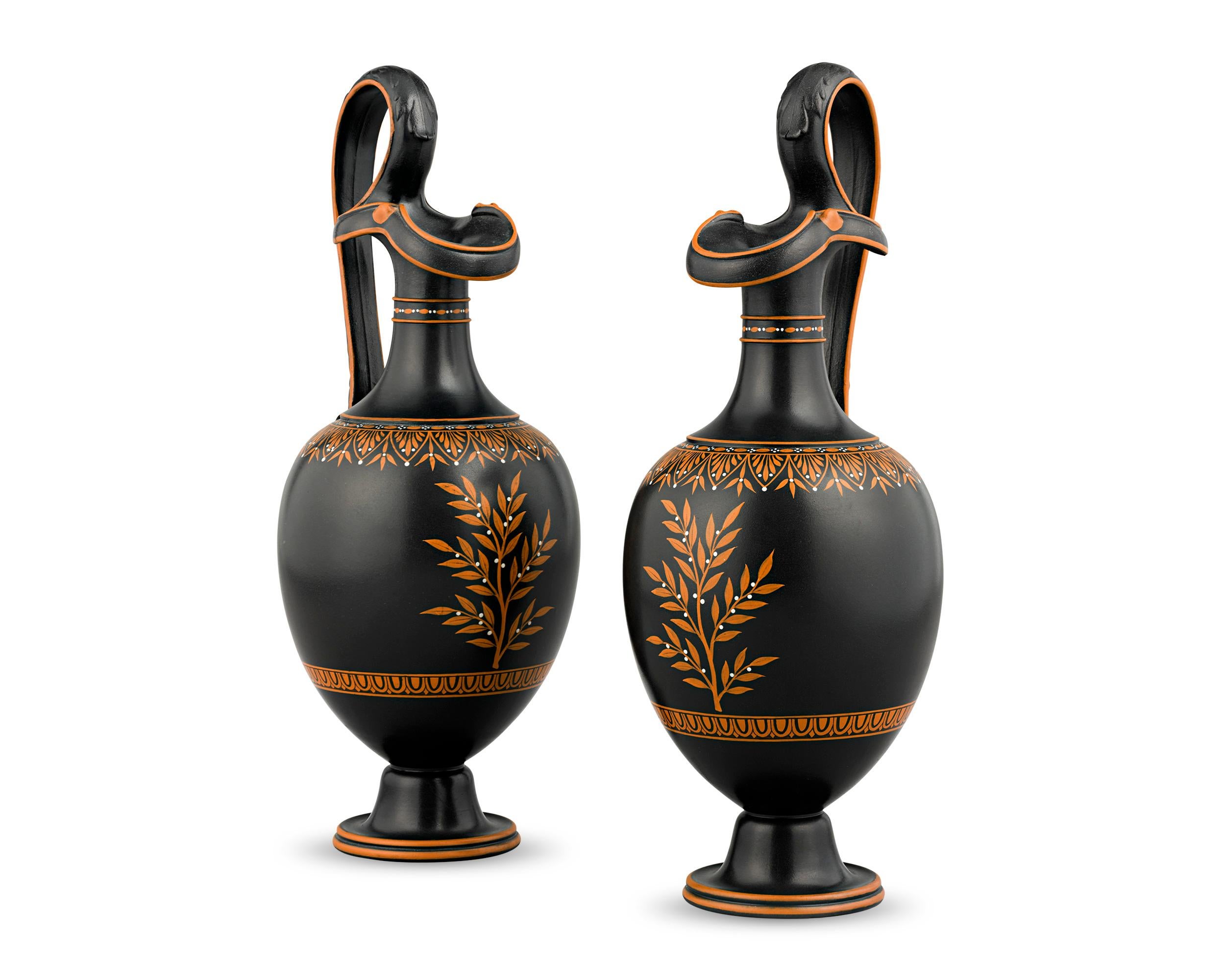 Crafted by Wedgwood, this pair of 18th century neoclassical oenochoe, or wine jugs, are comprised of black basalt — largely considered the firm’s greatest innovation. Decorations of terracotta red and white encaustic enamel adorn the handled vases,