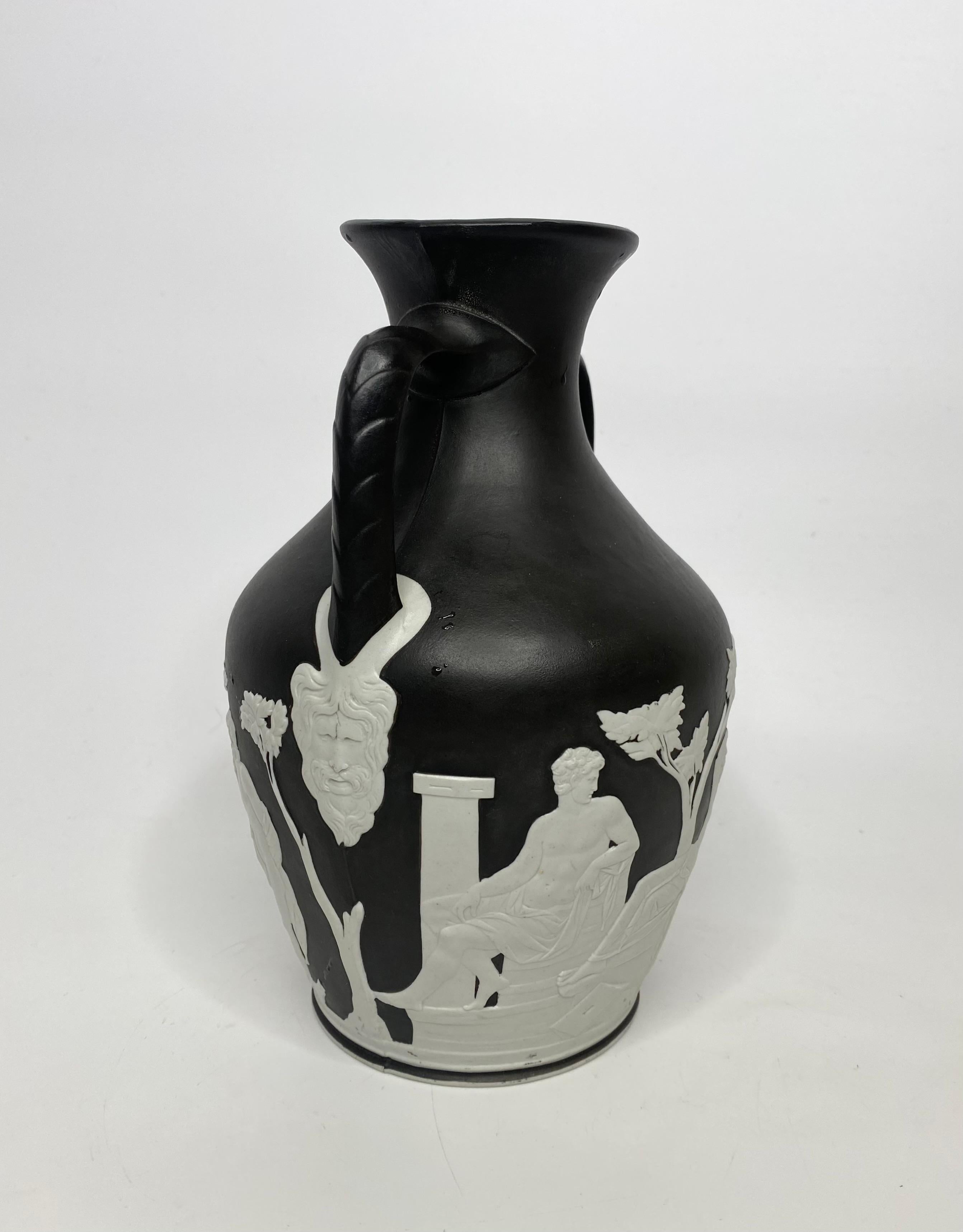 Wedgwood black basalt and white jasper ‘Portland Vase’, c. 1850. The classical form vase, decorated in white jasper relief, with a continuous Classical scene, of figures in a garden setting. The twin angular handles, terminating in bearded