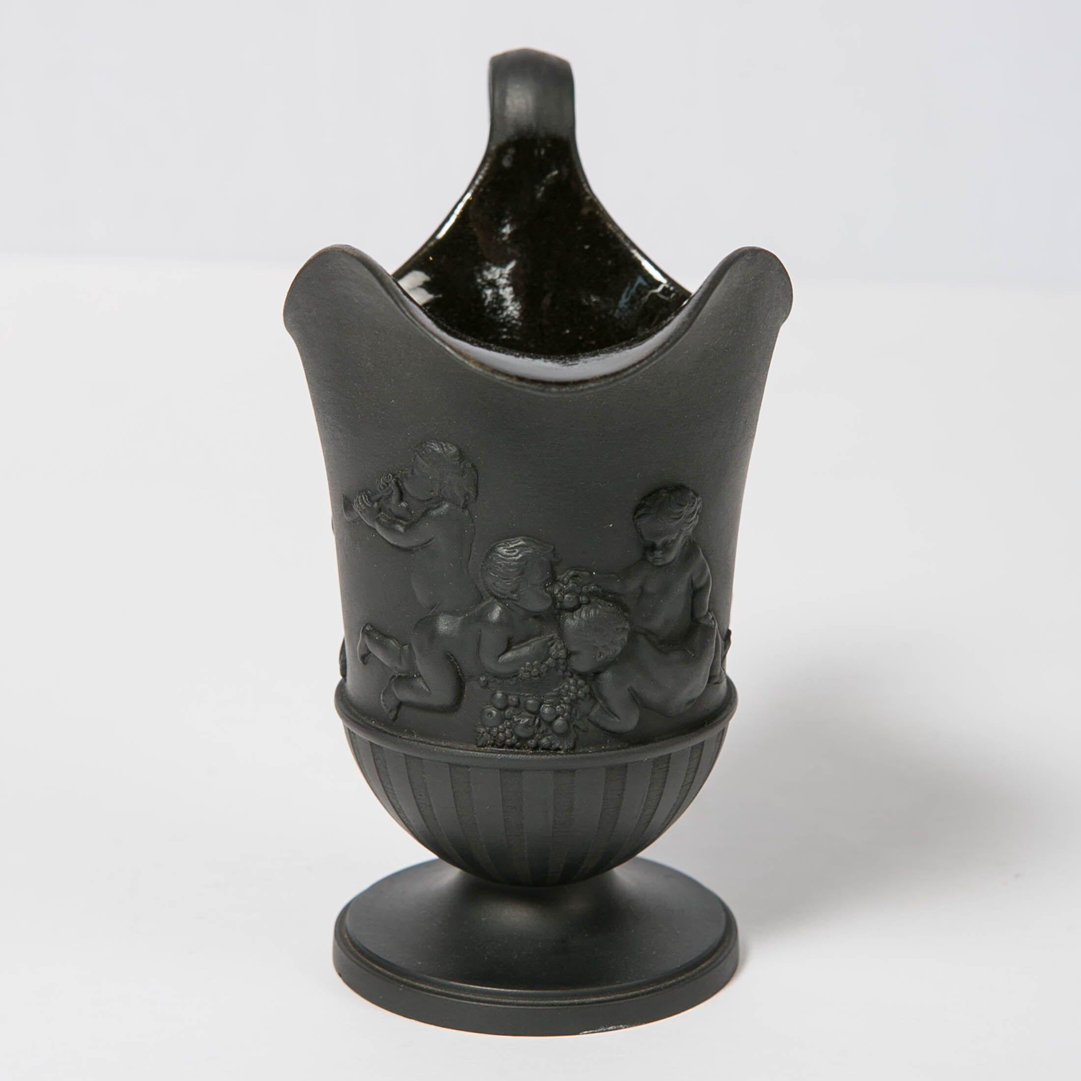 We are pleased to offer this Wedgwood black basalt helmet shaped pitcher. Made on a lathe with engine turning vertical lines rising from a round base. The pitcher is further decorated with embossed classical figures of children at play. It is