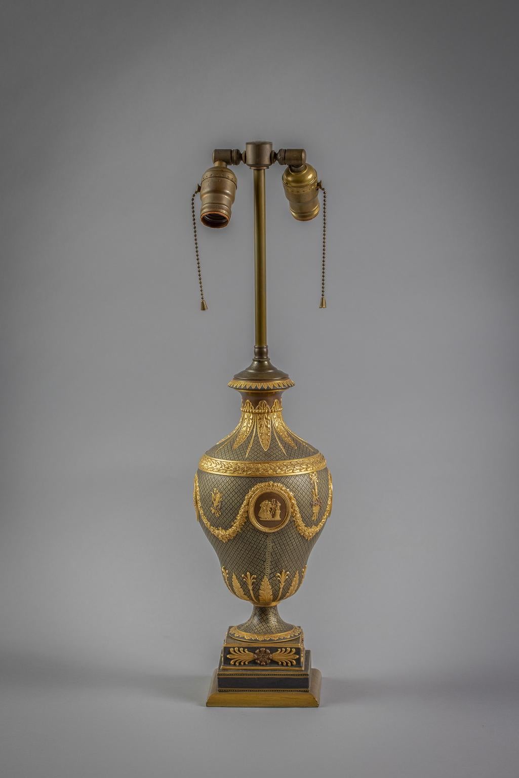 Mounted as a lamp, of ovoid form, decorated with oval medallions depicting classical figures on a gilt decorated black ground, hung with a floral garland continuing to a flared neck and removable lid, raised on a socle and ending in a square base.
