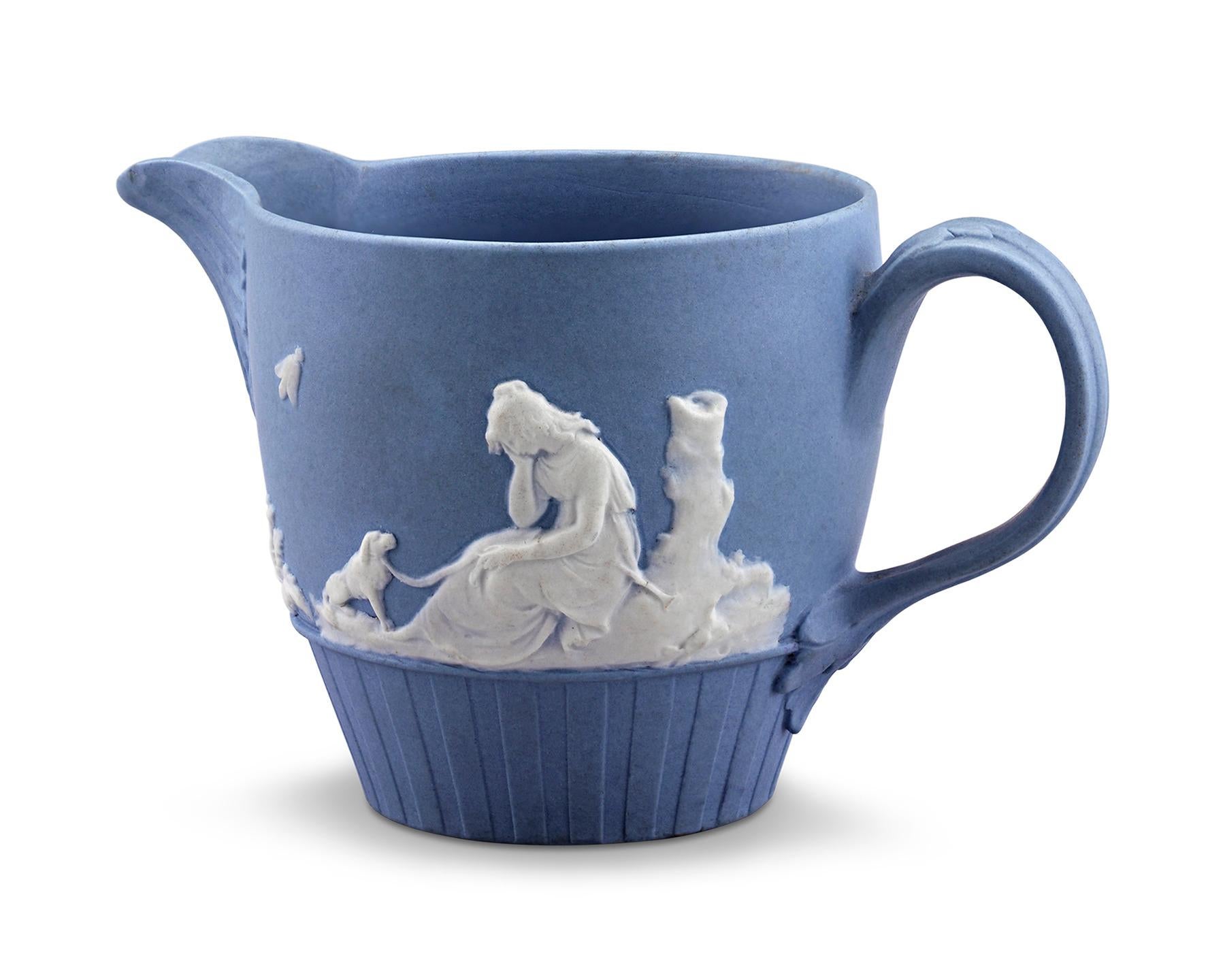 Crafted by Wedgwood, this diminutive creamer jug displays the firm’s iconic “Wedgwood blue” jasperware. A Neoclassical scene depicting a sorrowful goddess with her dog is silhouetted in bold white relief on one side, while the other side features a