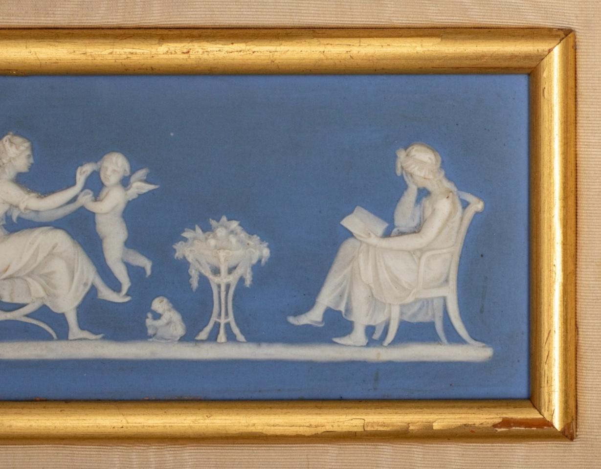 Wedgwood blue dip jasperware bas relief panel, likely late 19th century, and depicting classical women and children at study, rest, and play, now housed in a gilt and ebonized frame on sand moire ground. 

Dimensions: Panel: 3