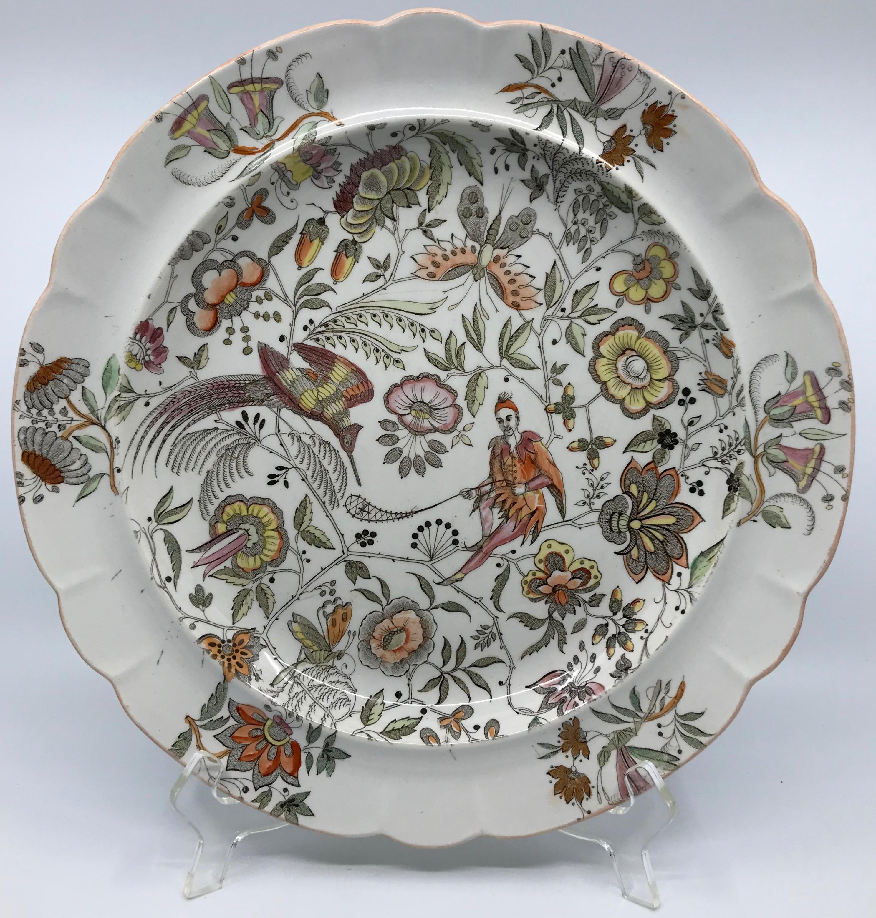 Wedgwood chinoiserie shallow-bowled plate with lobed peach slip edge. Fantastical rose apricot, peach and pale yellow and green decoration with fanciful oriental figure proffering a dragonfly to a long-billed bird surrounded by butterflies and