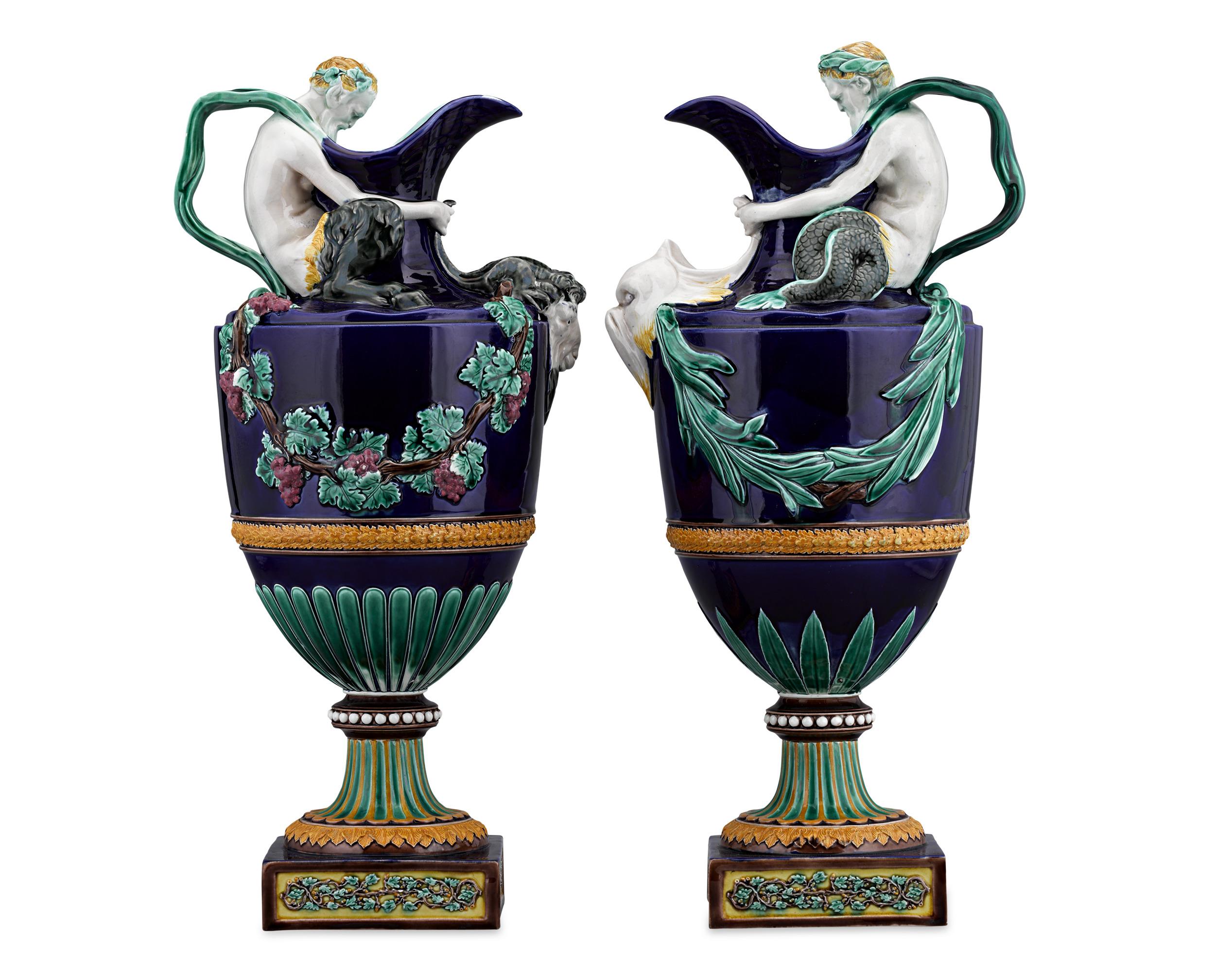 This breathtaking pair of wine and water ewers are made after models by John Flaxman. These exquisitely detailed and lushly rendered ewers are fashioned in a shield shape with sprayed foliate handles. The top of the water ewer is adorned with a