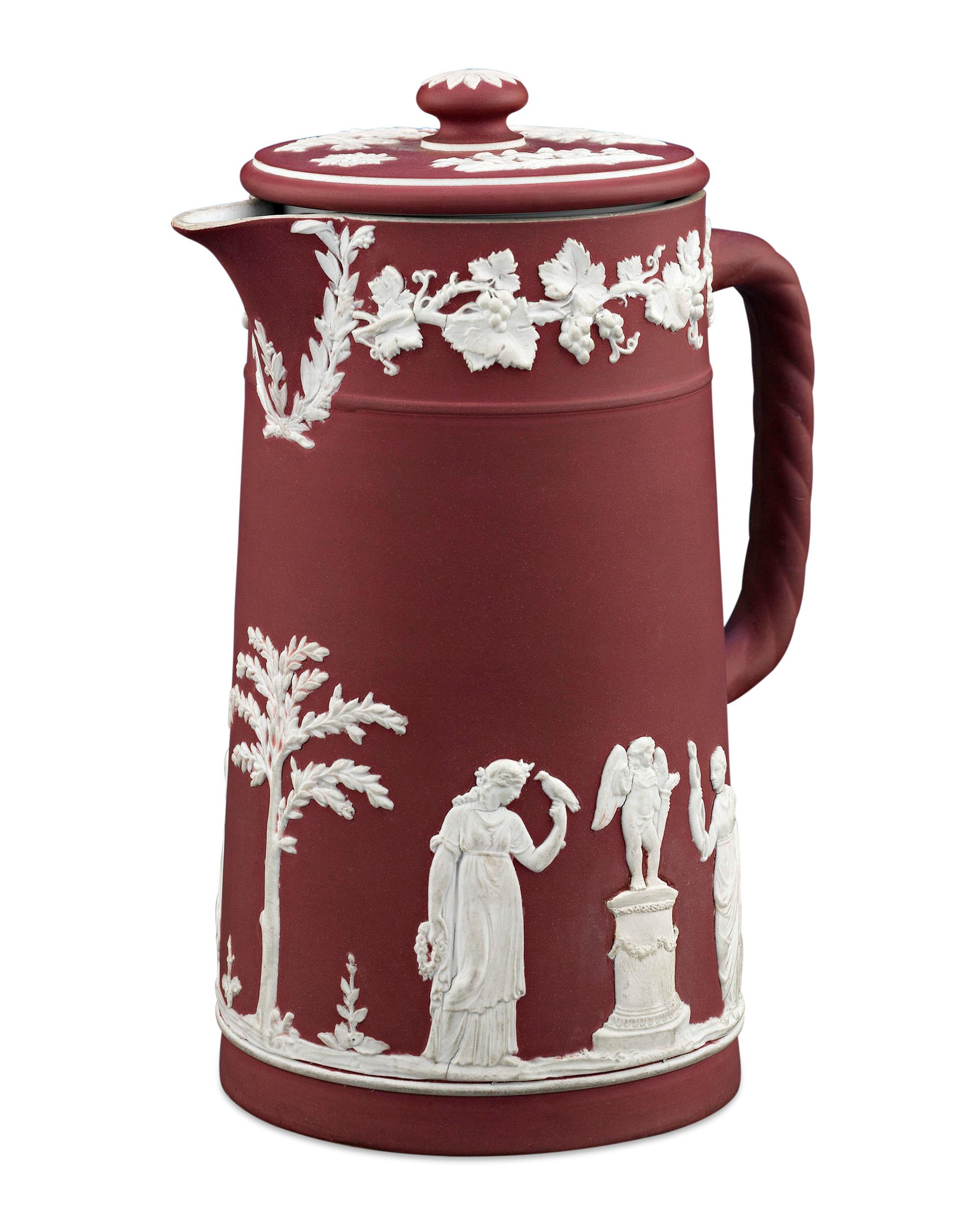 A lovely crimson jasperware jug by Wedgwood, featuring an applied white jasper neoclassical decoration of acanthus leaves and grapes bordering the rim. Maidens, children, and foliage provide the main focal point on the body. A twisted jasper handle