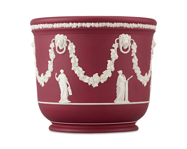The classical elegance of Wedgwood is showcased in this rare crimson jasperware jardinière. The highly prized vivid crimson hue of the vessel is beautifully accented by white flowered and ribboned garlands, while the draped Grecian figures of the
