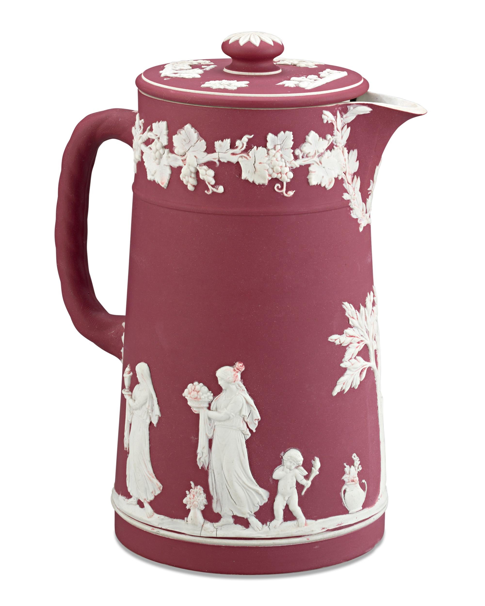 This striking Wedgwood crimson dip bas-relief covered jug features an applied white jasper neoclassical decoration of grapevines bordering the rim. Delicately rendered maidens, children and foliage encircle the pitcher’s body, providing wonderful