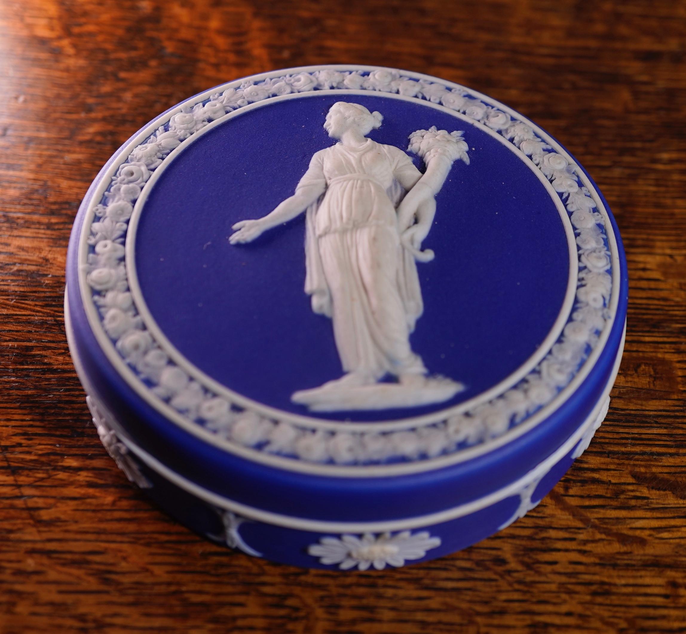 Wedgwood deep blue jasper round box, the lid with a white sprigged figure of 'Flora' with cornucopia of flowers, within a sprigged wreath, the base with daisy heads and bell flower frieze.
Impressed. WEDGWOOD and 'M',
circa 1815.