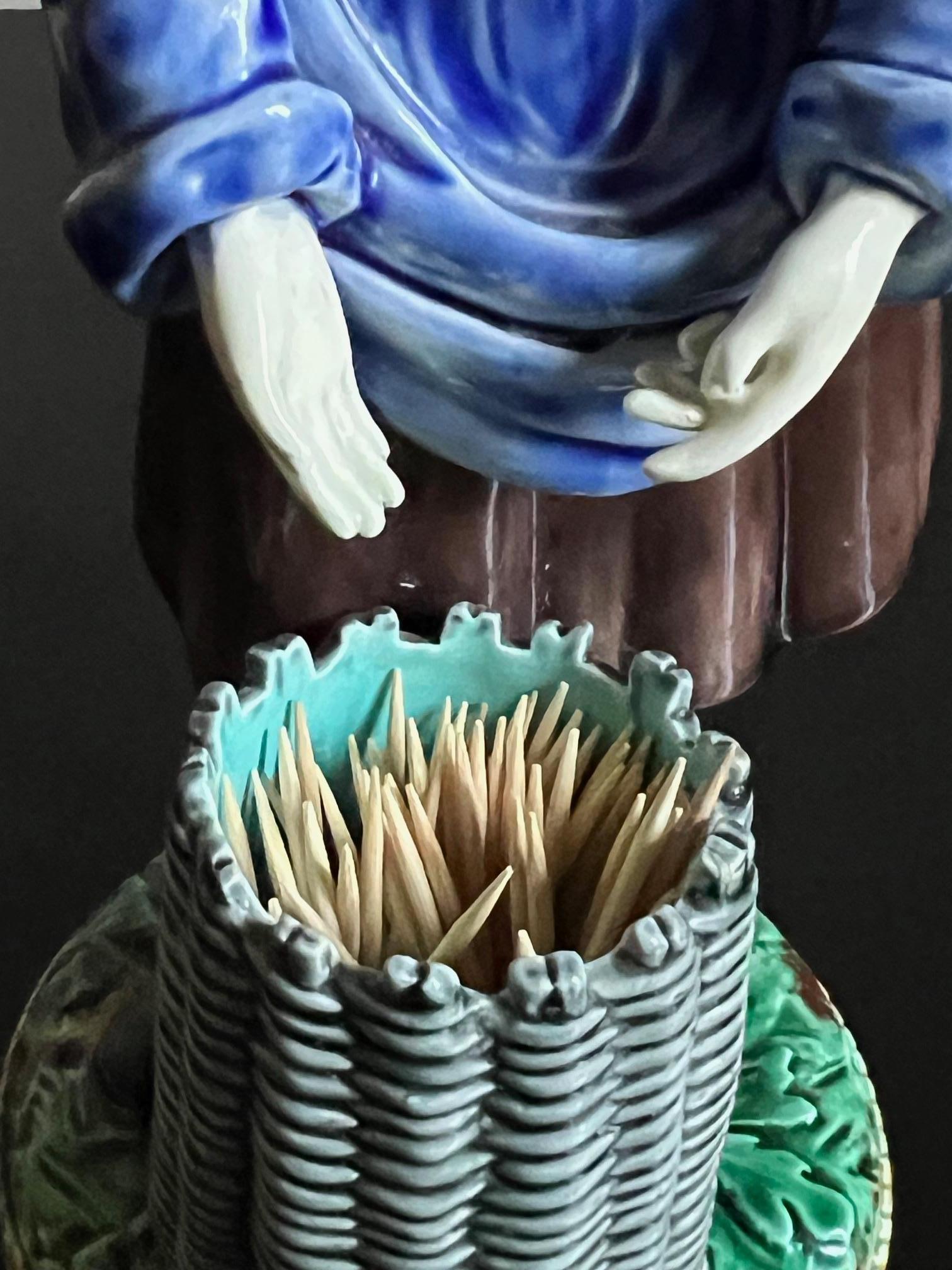 Antique majolica figure with a basket made in England by Wedgwood in 1873. She is a fisherwoman wearing traditional clothing, bent over a turquoise lined basket, it is pattern M 1210.


