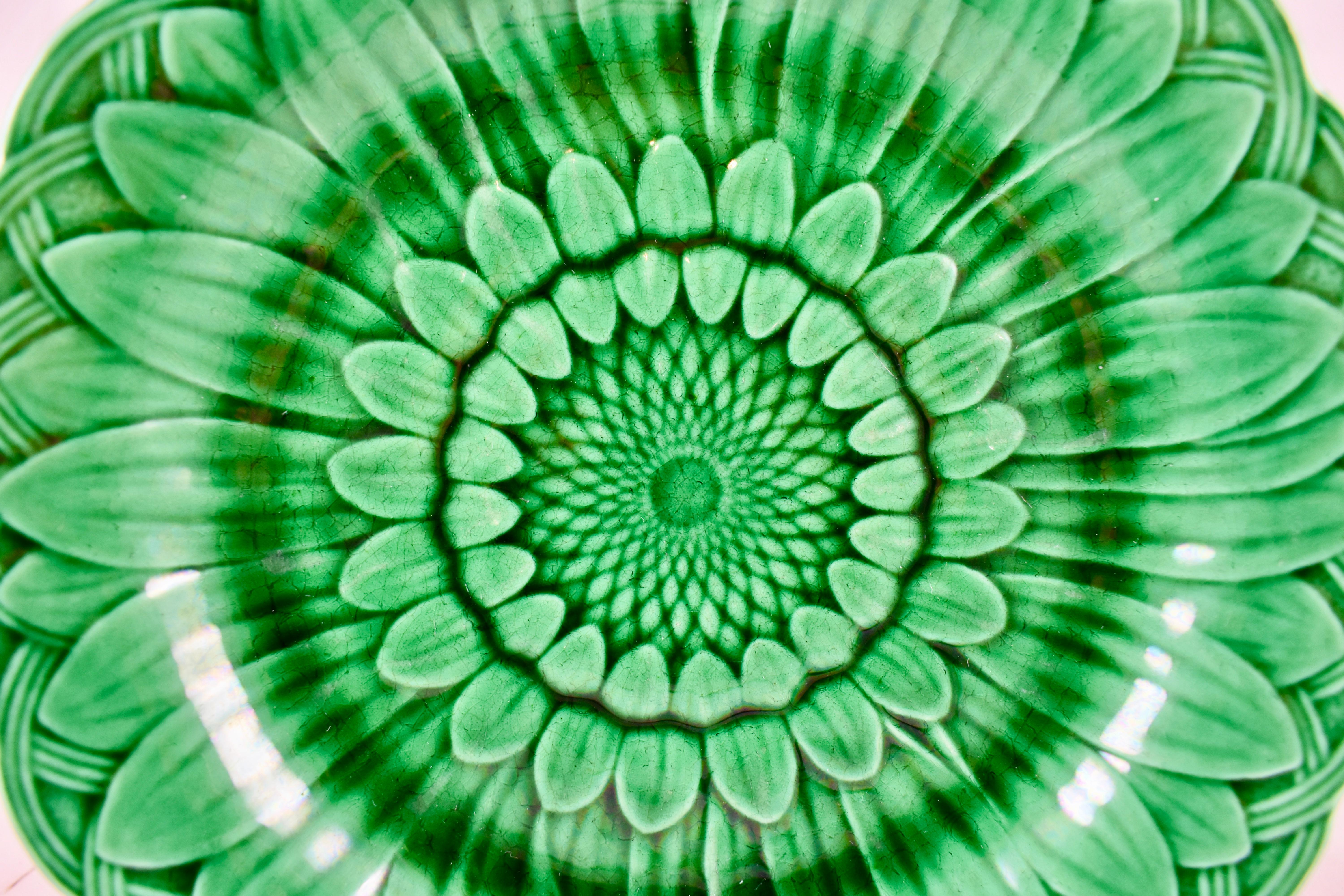 A majolica green glazed plate, from the English firm of Wedgwood. 

A classic mold showing a sunflower head against a basket-weave shaped rim. The deep green glaze pools beautifully into the dimensional mold work.

Measures: 8.75 in. diameter x