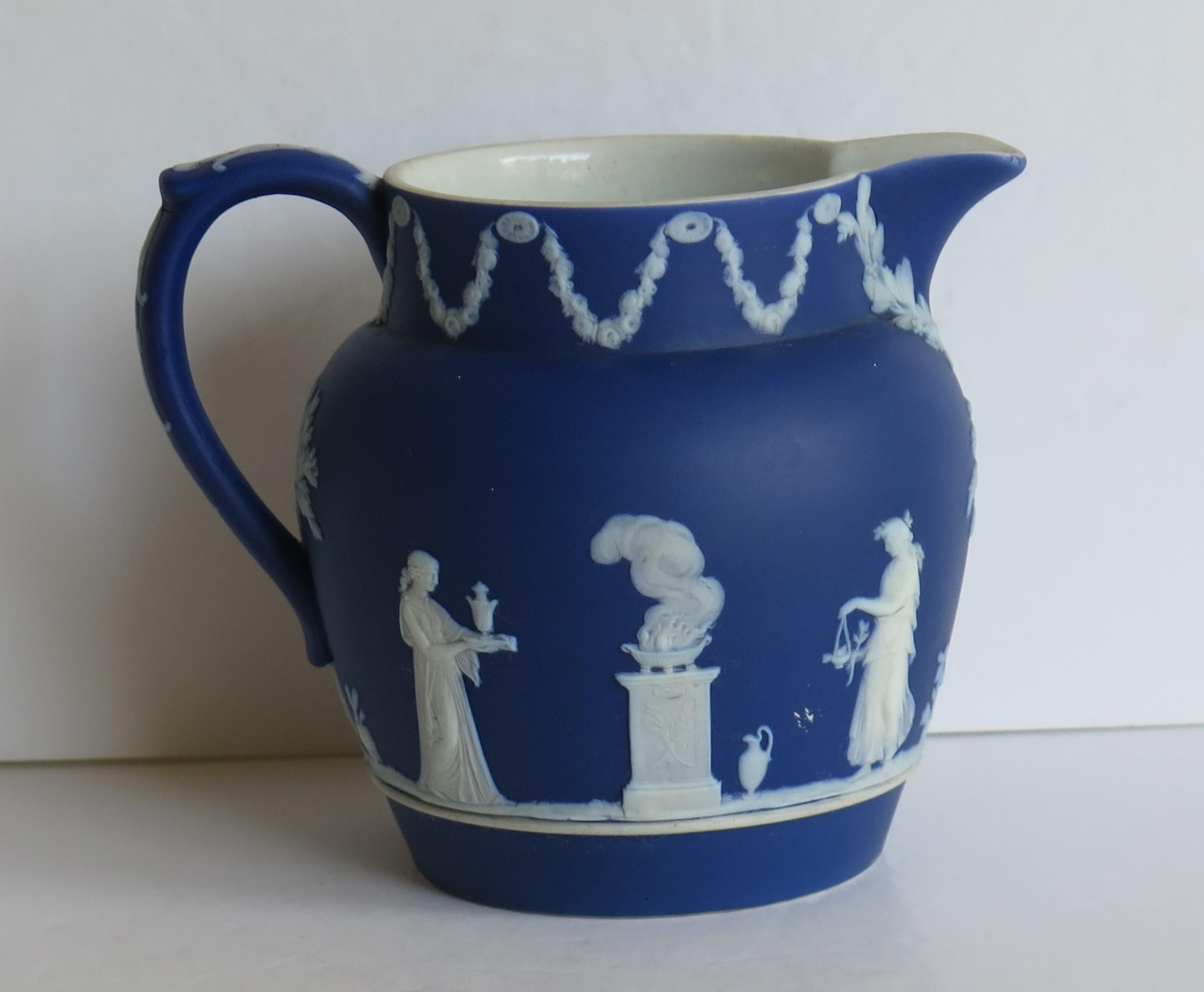 This is a good Jasperware stoneware jug or pitcher, made by Wedgwood, England and dating to circa 1900. 

The jug has a lovely shape with a pouring spout and loop handle.

The jug has a classical figures pattern, the figures being applied relief