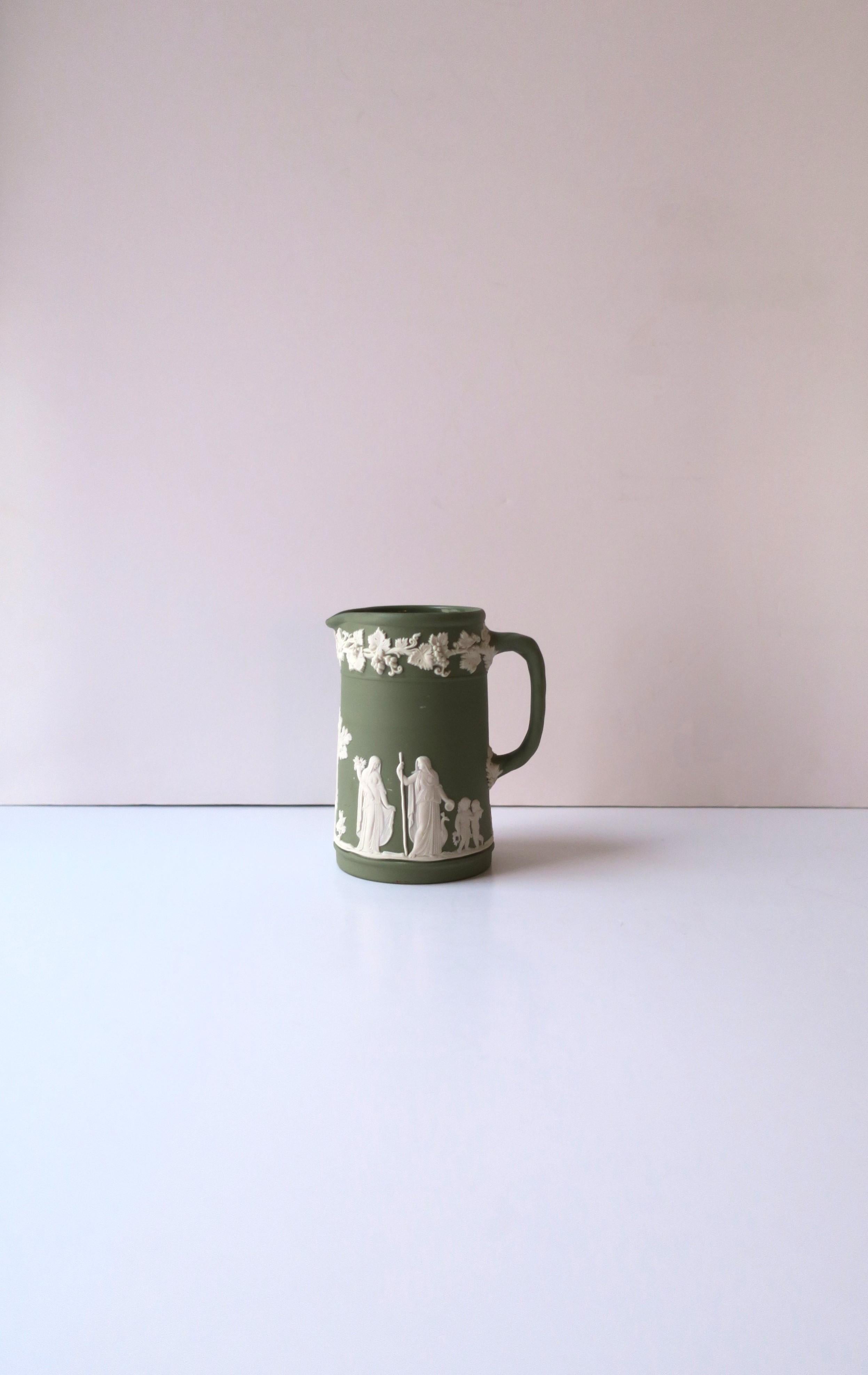 An English sage green and white Jasperware matte stoneware pitcher by Wedgwood in the Neoclassical style, circa early-20thth century, England. Pitcher has a white raised relief of grapes, leaves and vines, around top, base and center area have