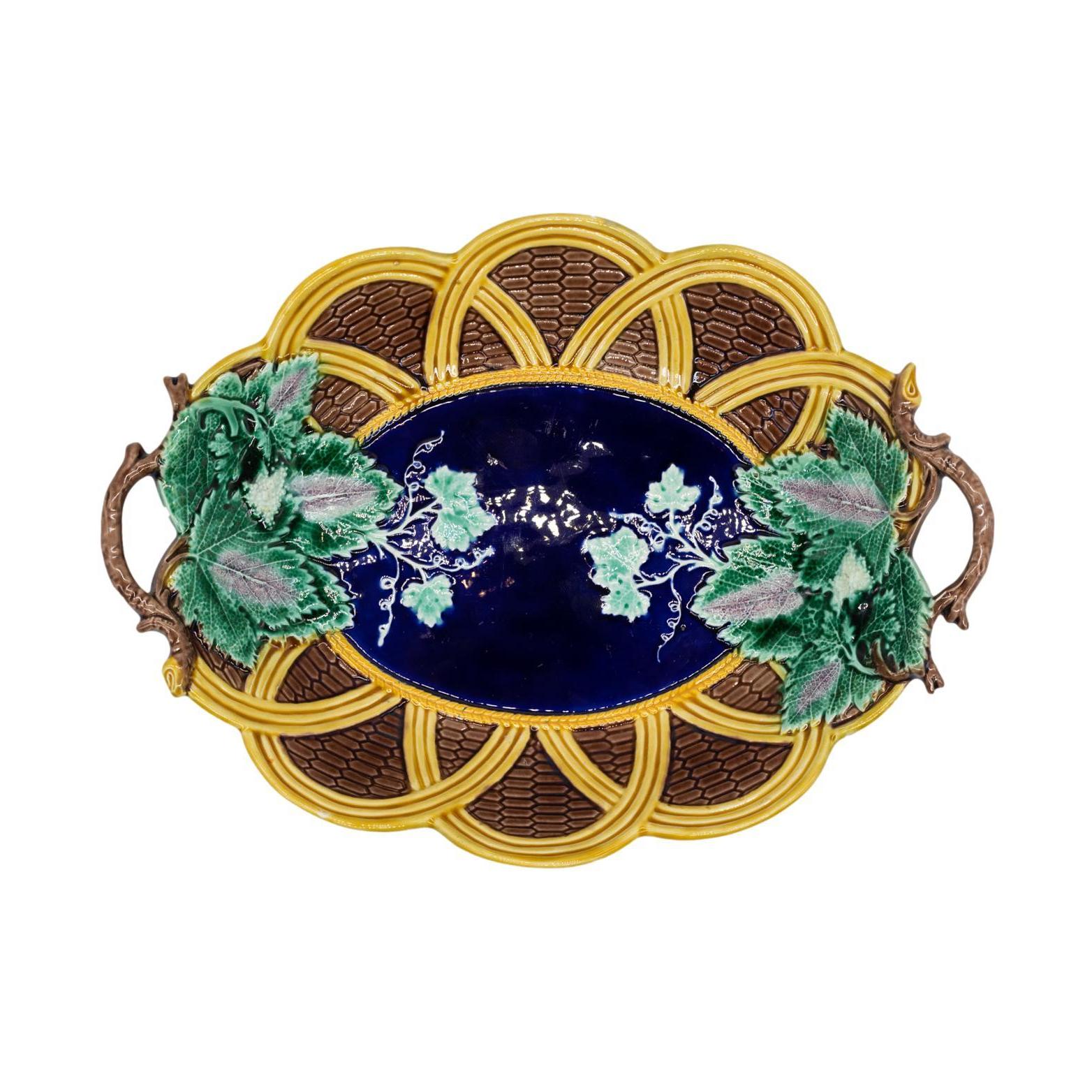 Wedgwood Majolica scalloped oval bread tray, molded as a shallow looped wicker basket, the center glazed in cobalt blue and bordered in yellow-glazed wheat with green, lavender, and white grape leaves and tendrils to either side, surmounted with