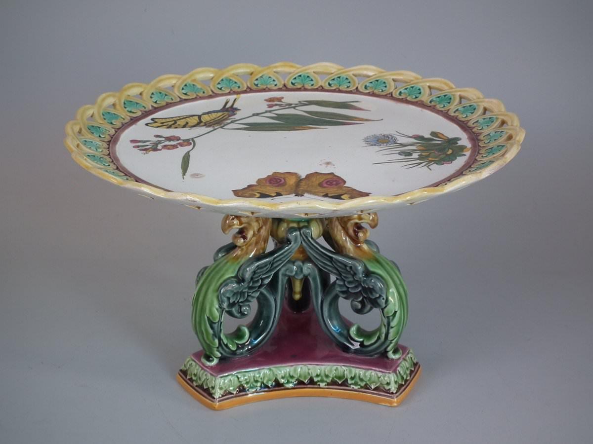Wedgwood Majolica compote which features a printed zoological study of butterflies and flowers. The foot features eagle heads. Coloration: white, green, yellow, are predominant. The piece bears maker's marks for the Wedgwood pottery. Bears a pattern