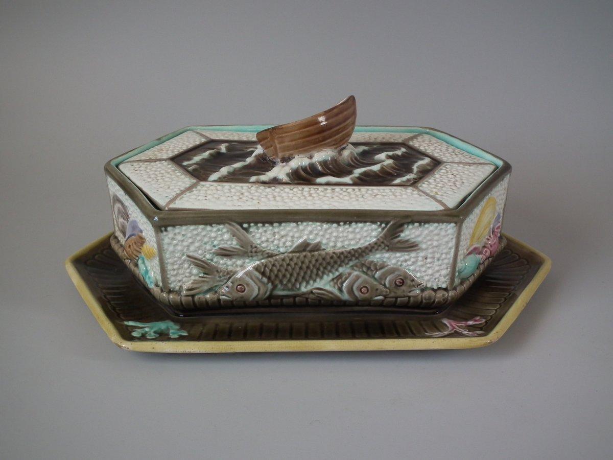 Wedgwood Argenta Majolica sardine box which features rolling waves, fish, shells, coral and a boat handle to the cover. Coloration: cream, brown, pink, are predominant. The piece bears maker's marks for the Wedgwood pottery. Marks include a factory