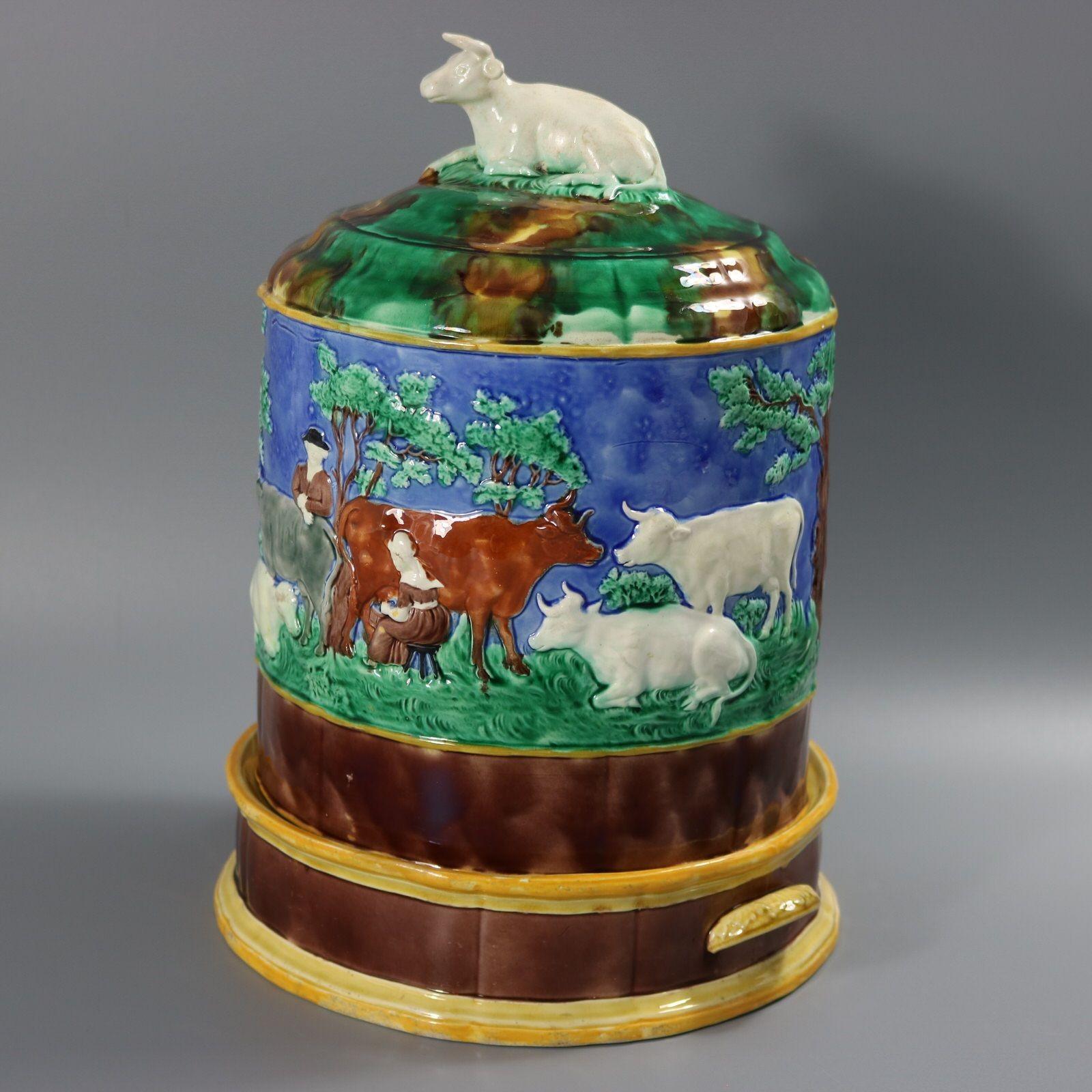 Guarda quesos de mayólica Wedgwood que presenta una escena campestre en el exterior, con vacas, granjeros y una criada ordeñando. La parte superior tiene un remate de vaca. Coloración: predominan el azul, el verde y el blanco. La pieza lleva marcas