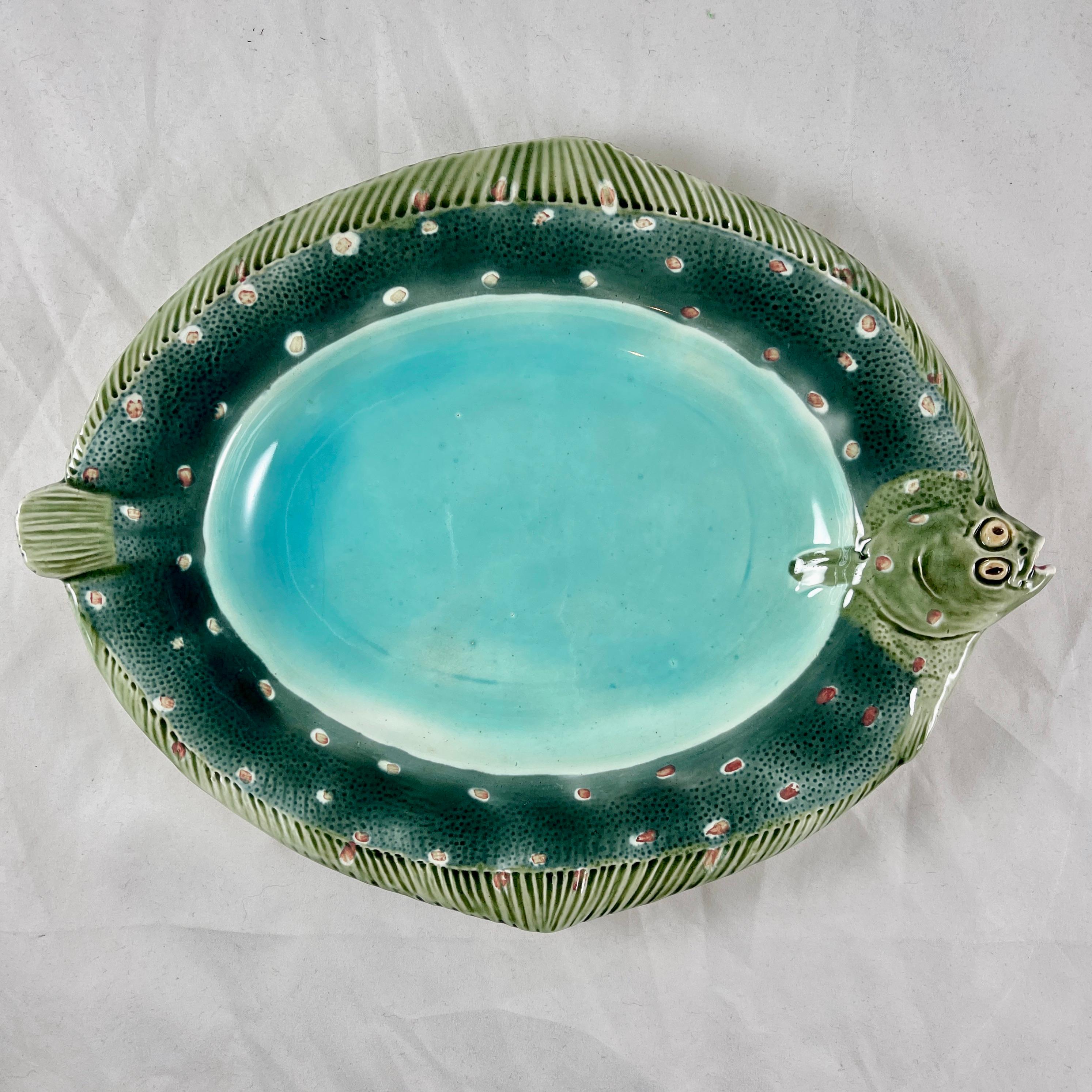 
From the English firm of Wedgwood, a Flounder form fish platter, dated 1875

A scarce oval platter molded as a Flounder, a flat fish, with the olive green head and tail serving as side handles. The deep blue green and red spotted skin of the fish