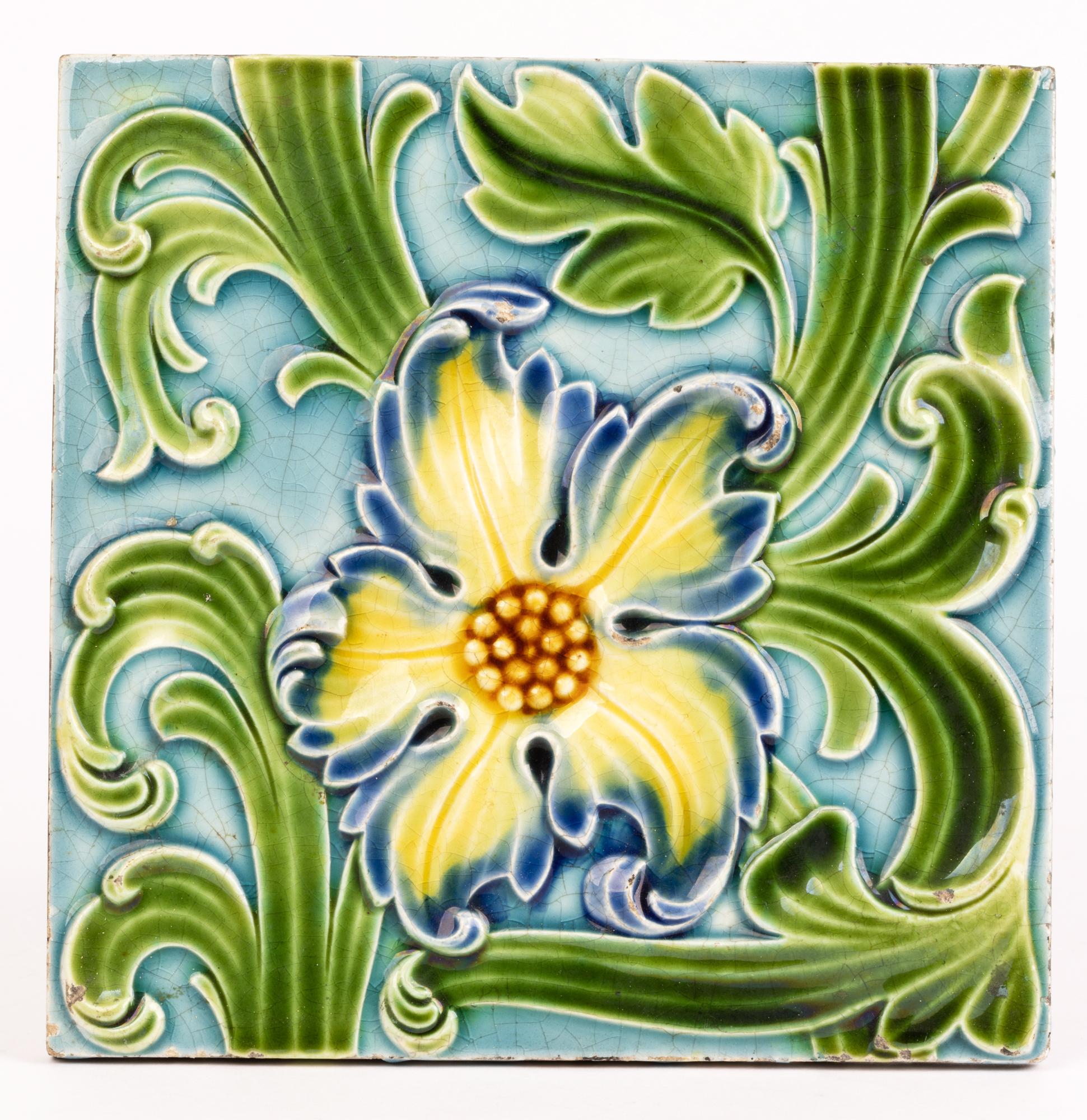 A large and impressive antique Wedgwood majolica tile decorated with a floral design dating from the 19th century. The tile of square shape is molded in relief with a central floral bloom set amidst green stems. The tile is hand decorated in colored
