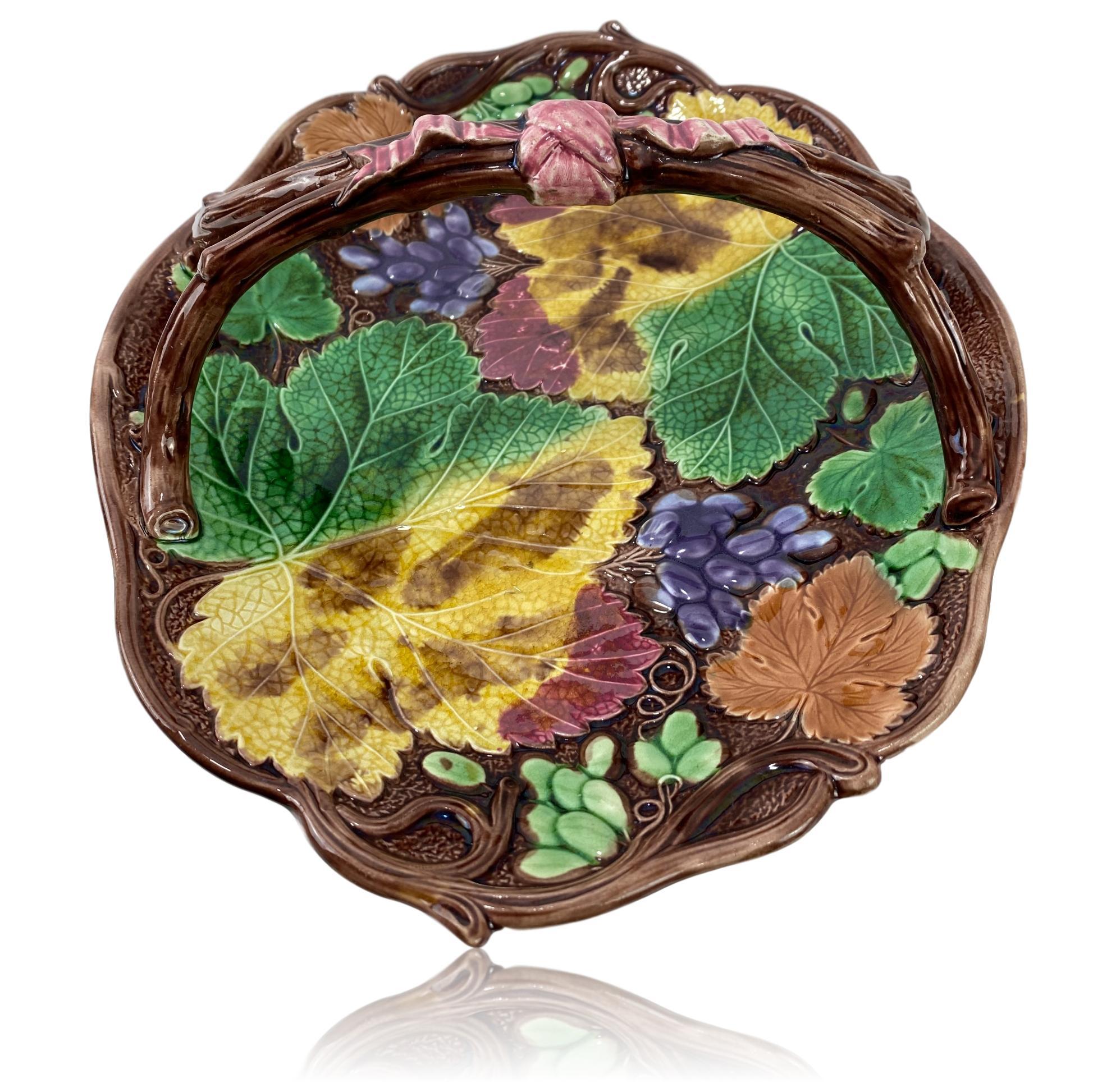 Wedgwood Majolica 'Colored Vine Bread Basket,' English, dated 1874, naturalistically modeled as a shaped oval dish bordered with grapevines, with purple and green grapes on a bed of autumn leaves, with simulated twigs forming the handle, surmounted