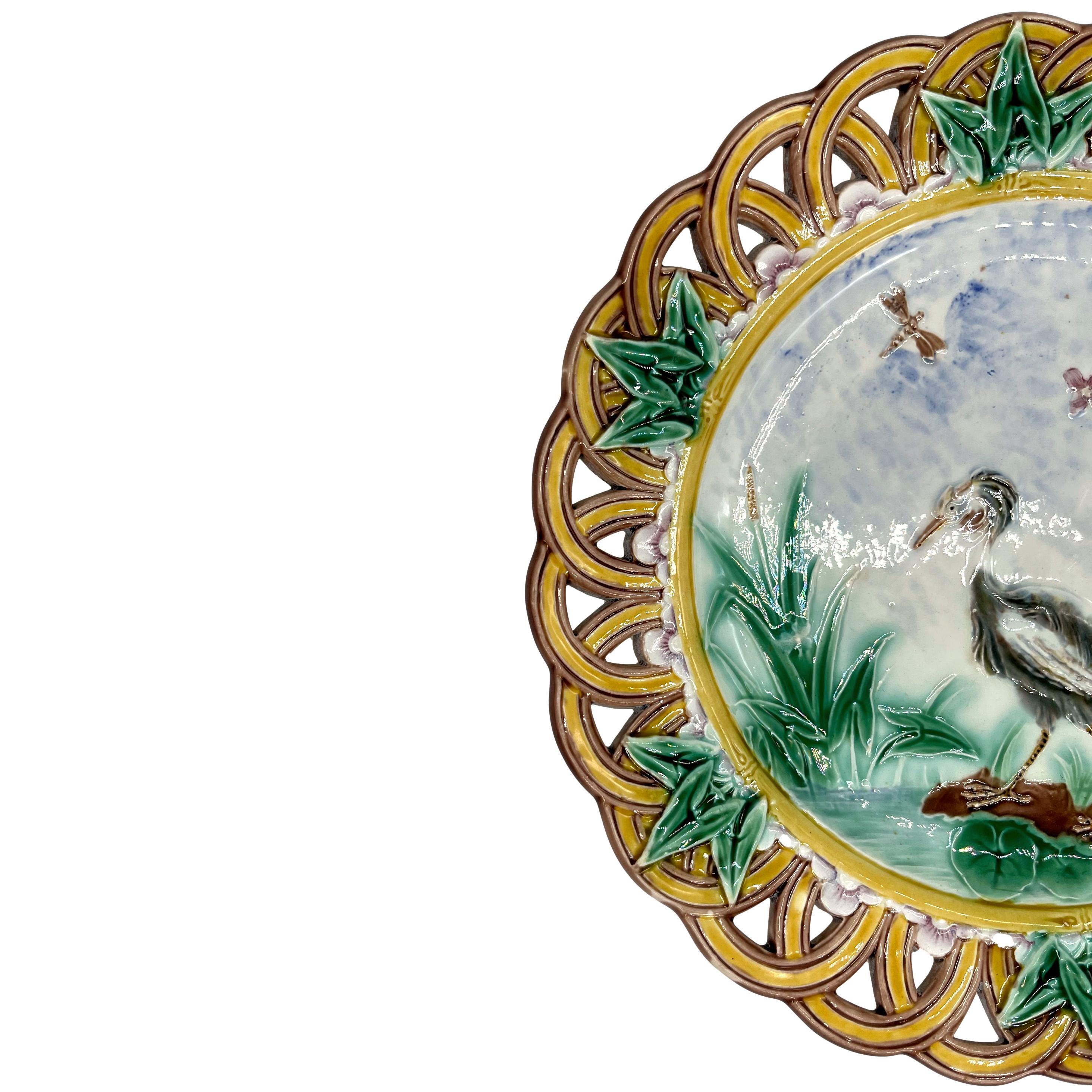 A Wedgwood Majolica 9-in Plate, the center with a relief-molded stork, waterlilies, cattails, and pink-tinged blossoms, and a single dragonfly, the cavetto with a relief-molded and yellow-glazed bamboo border, the lip with a band of molded blossoms