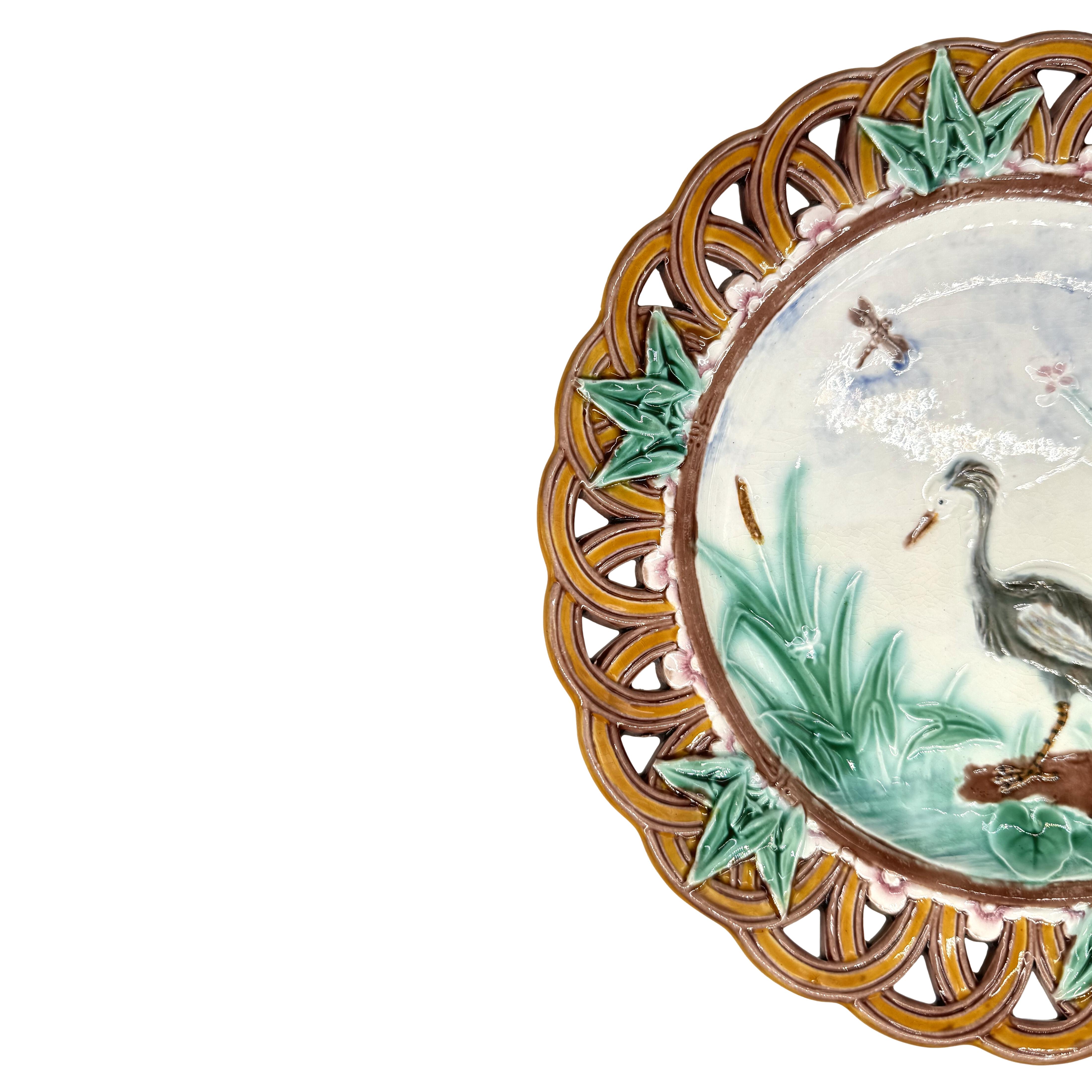 A Wedgwood Majolica 9-in Plate, the center with a relief-molded stork, waterlilies, cattails, and pink-tinged blossoms, and a single dragonfly, the cavetto with a relief-molded and yellow-glazed bamboo border, the lip with a band of molded blossoms