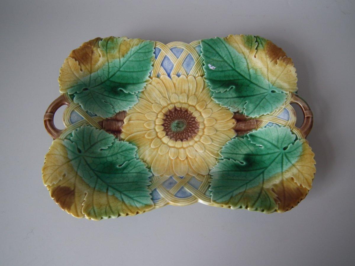 Wedgwood Majolica platter which features a sunflower in a basket. Coloration: green, ochre, brown, are predominant. The piece bears maker's marks for the Wedgwood pottery. Marks include a factory specific date cipher for the year 1861.
