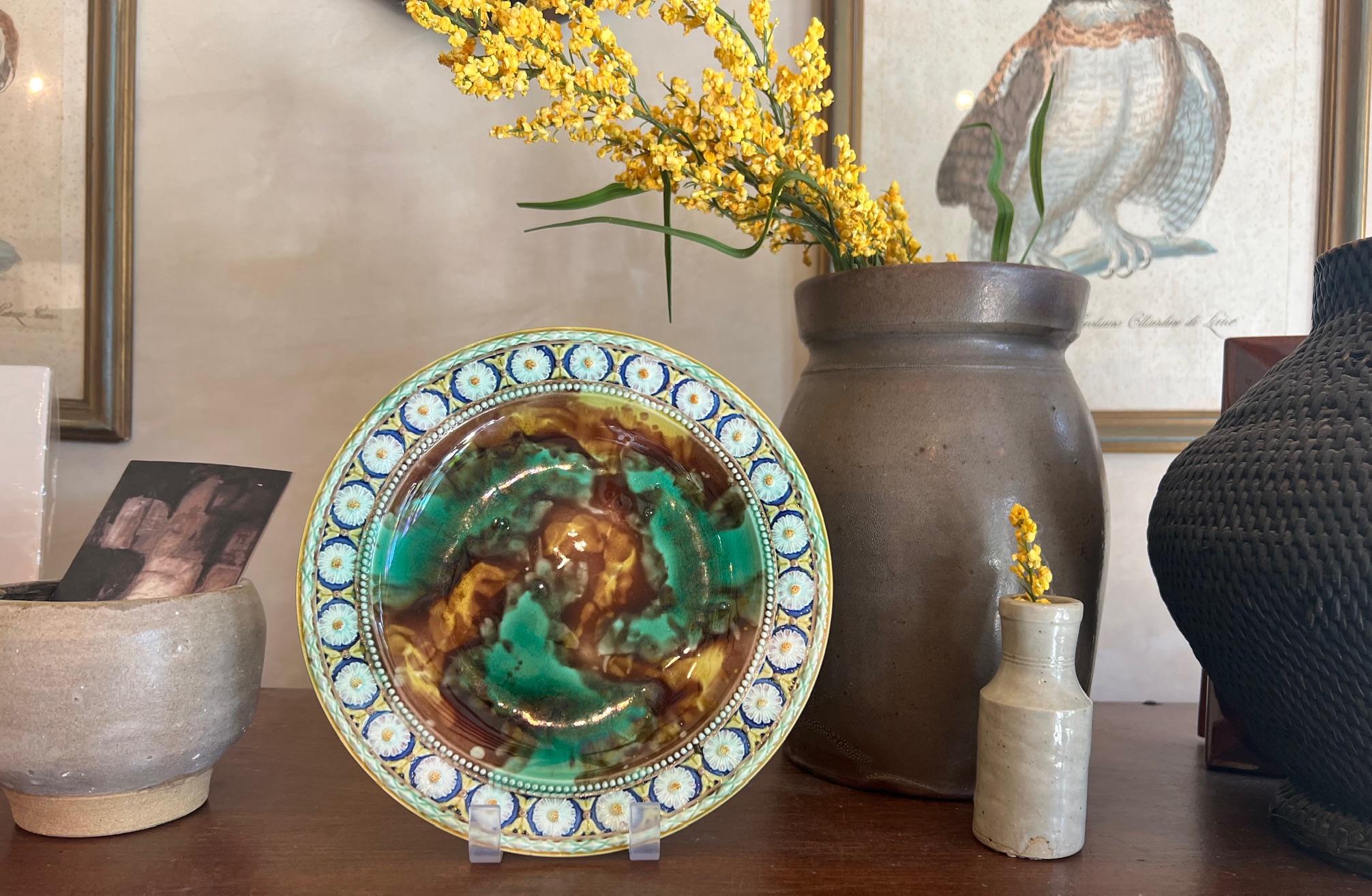 Set of two antique majolica plates by Wedgwood in England in 1871 and 1872. The ceramic plates have a molted tortoise shell design in the center surrounded by a ring of daisies, separated by a beaded border. They are both hand painted so not exactly