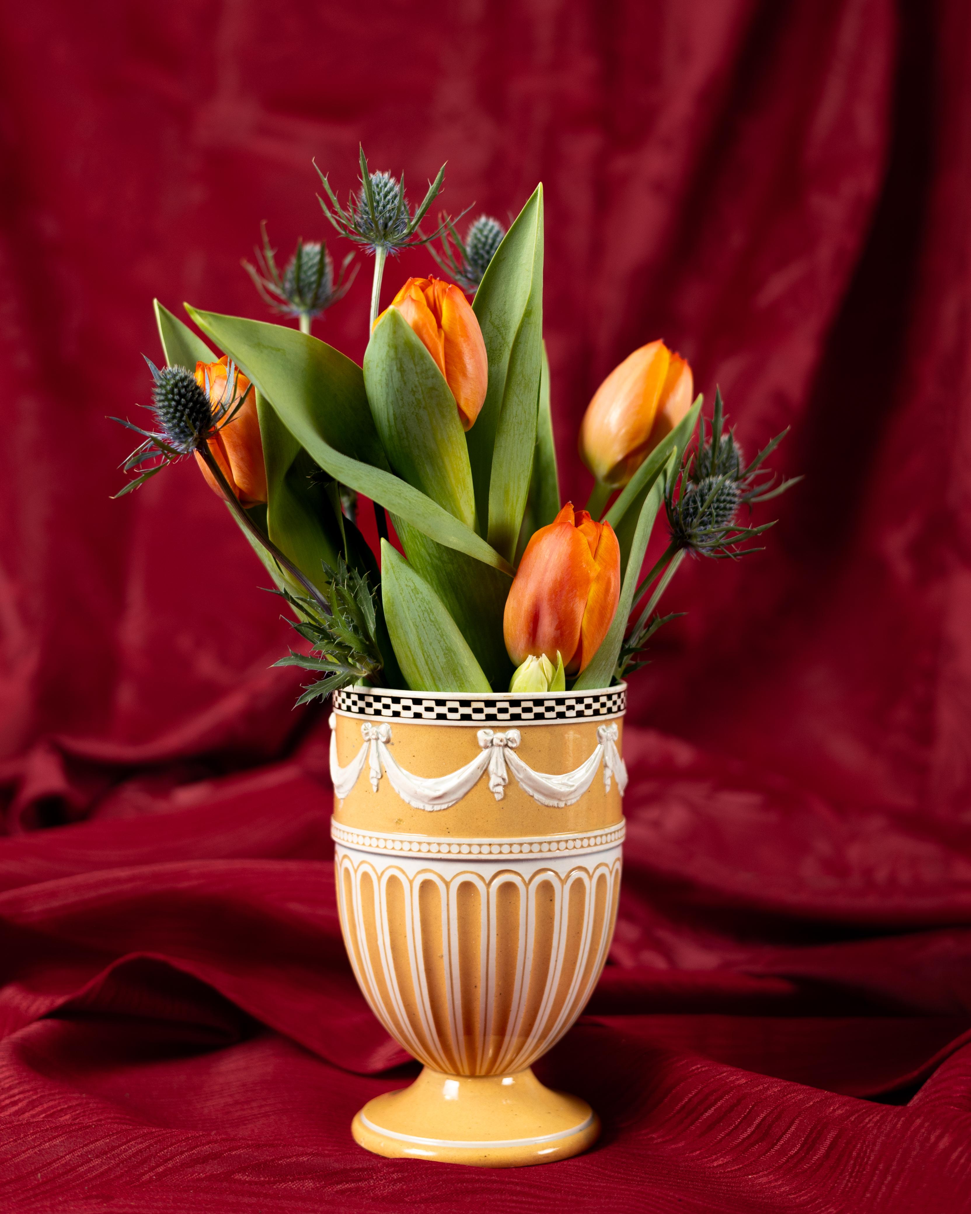 This early 19th century Wedgwood slip decorated vase has an elegant design.
It is decorated with ochre-colored slip on the outside and features unpainted white grooved columns that rise to a band of white 
