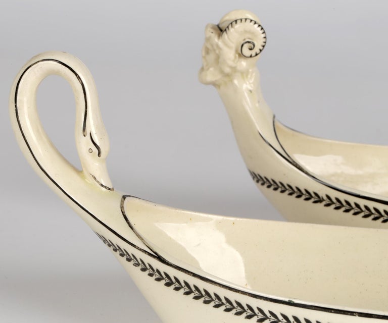 An unusual and scarce pair Wedgwood creamware sauce boats or dishes with swan neck handles and raised molded Bacchus heads dating from 1912. The dishes are lightly potted and are simply decorated with black spot outlines and feathered pattern around