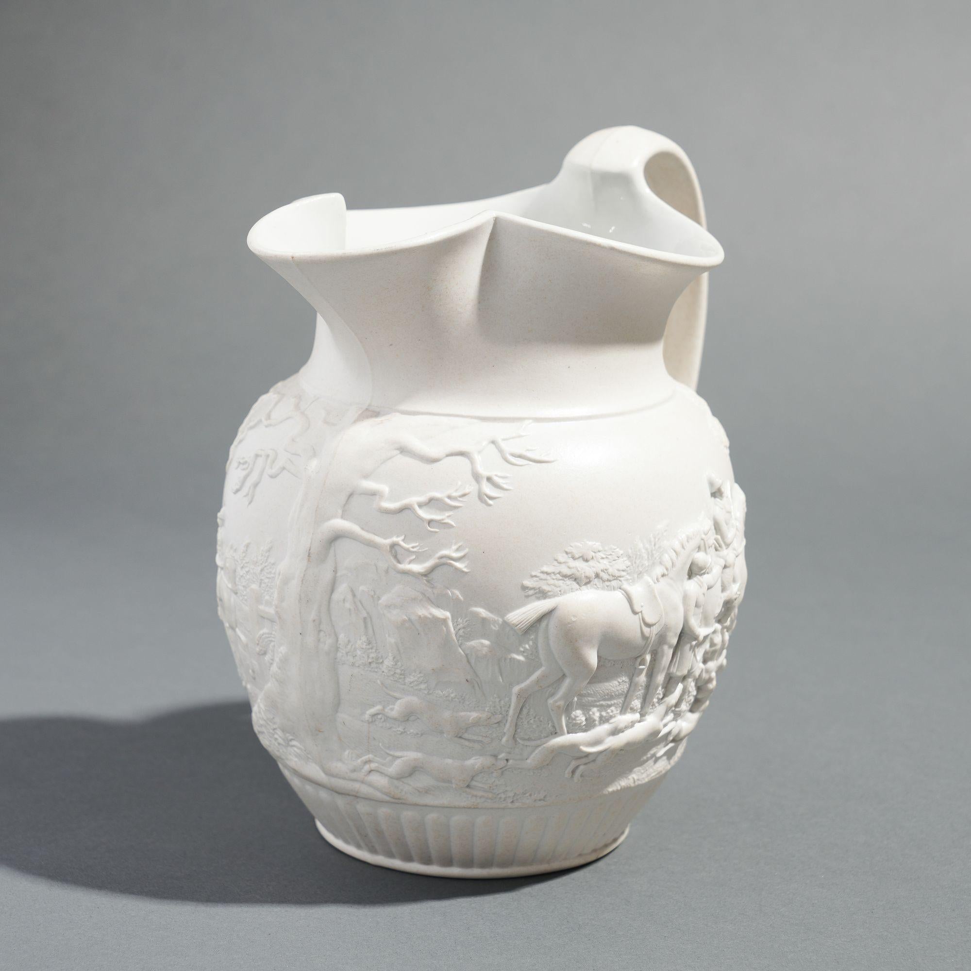 Stoneware hunt jug with a white smear glaze and applied loop handle. The raised and highly detailed hunt scene encircles the jug above a reeded base.

Stamped on the underside: Wedgwood
A 