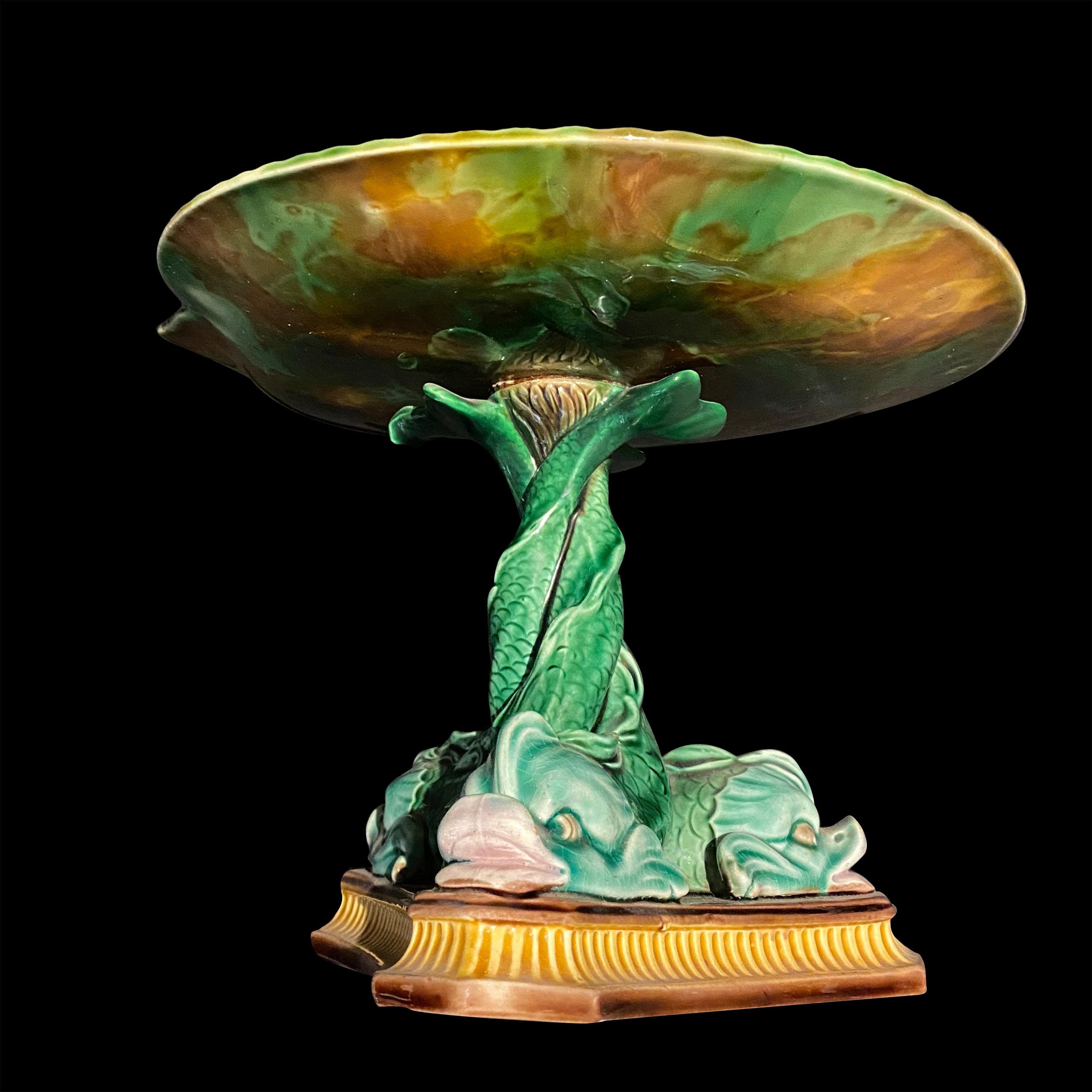 This Wedgwood tazza is decorative Delphin is a brightly decorated compote presented as a large clamshell mounted on three dolphins on a three-point base. In typical Majolica colors, precise and well-sculpted (as it is at the beginning of the mold