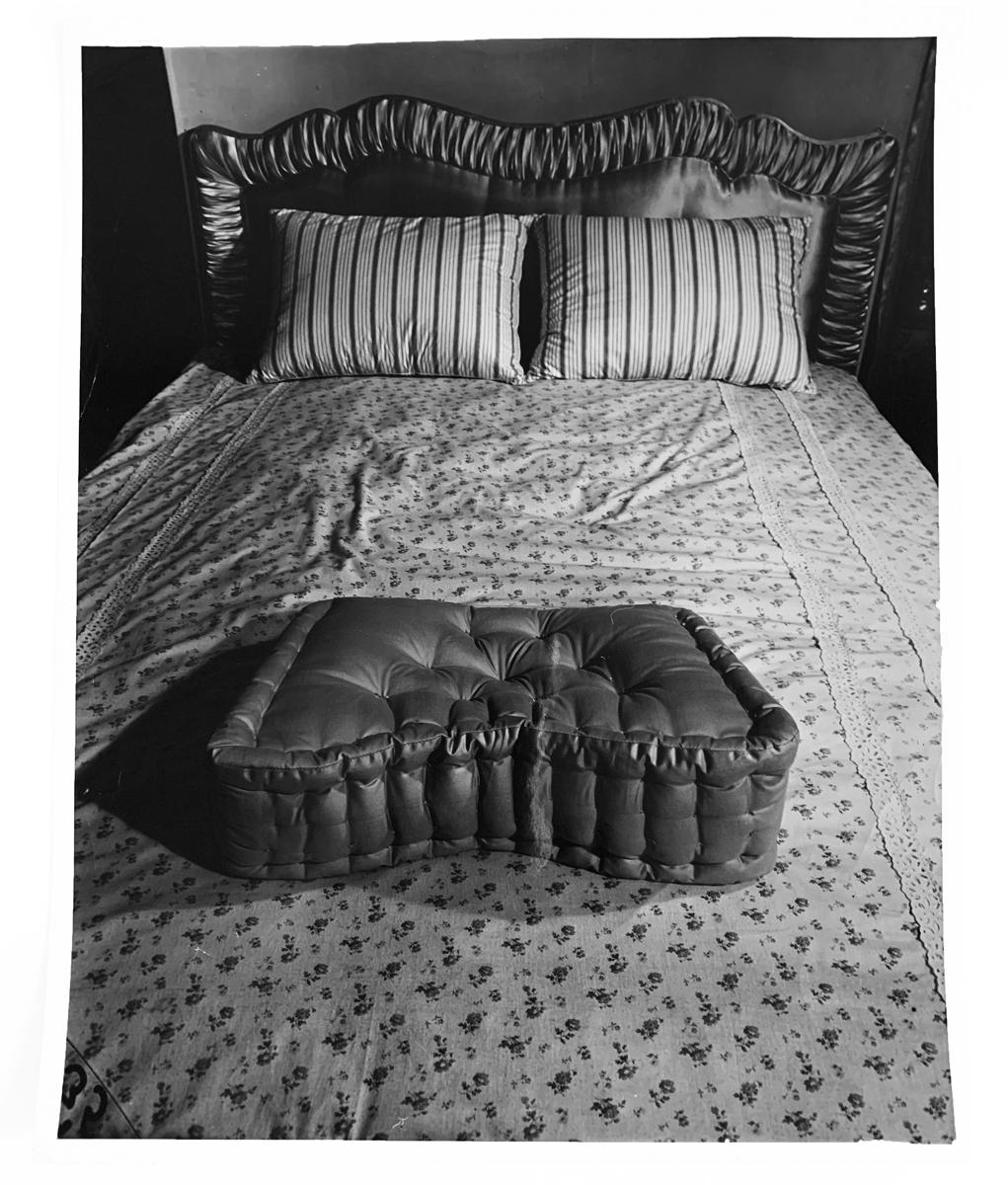 Bundling bed and pillows, c.1950-60, by Weegee -- paper size: 14" x 11" and image size: 13 1⁄2" x 10 5⁄8" -- is a gelatin silver print with Weegee's copyright stamp on back of photo. Weegee, who shot film using a Speed Graphic 4 x 5 camera, learned