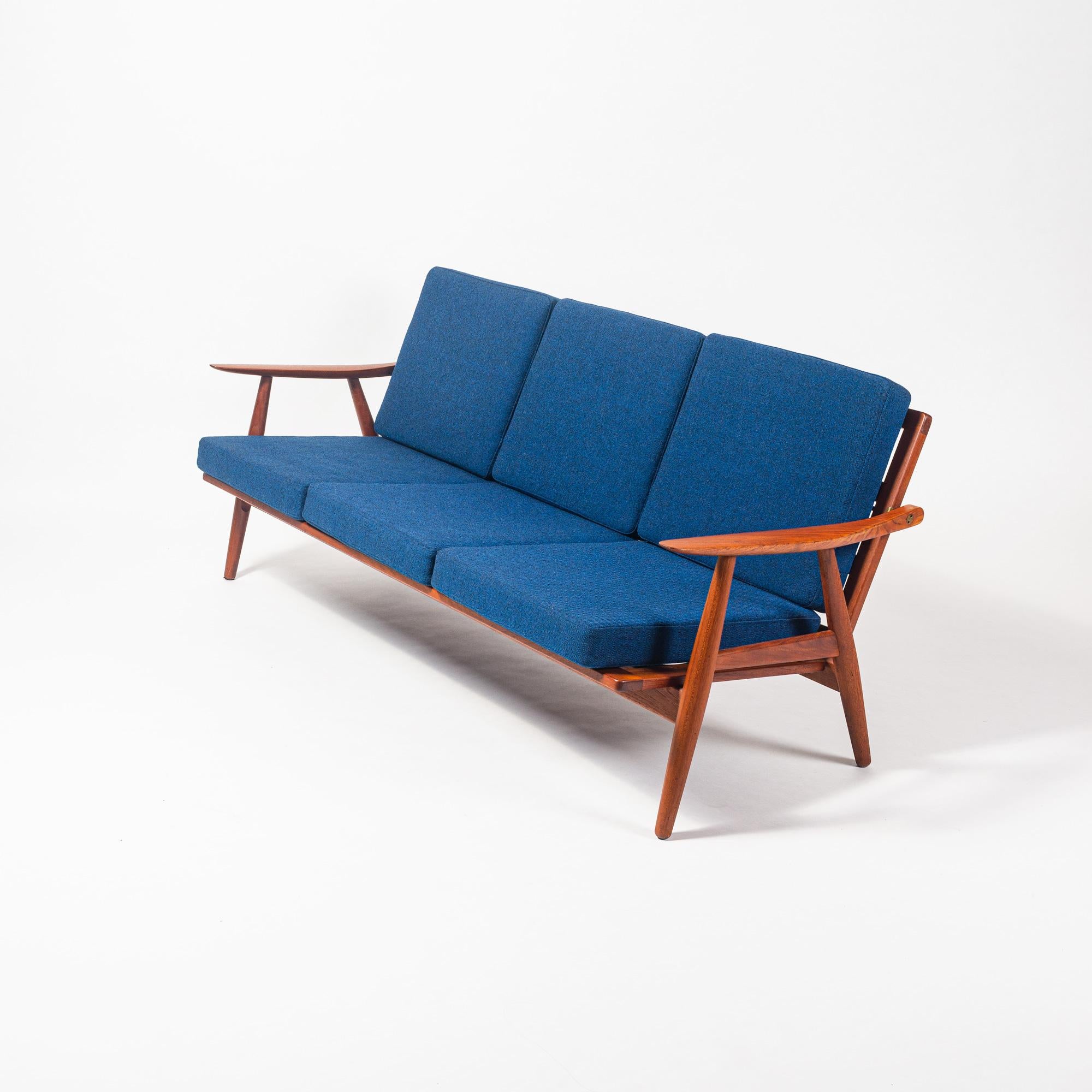 A Hans Wegner GE-270 three seater sofa in solid teak and new royal blue wool upholstery, circa 1950s. This sofa has a sculpted solid teak frame with exposed, bespoke brass fittings. Unlike the Wegner Cigar Series or other series, this model has