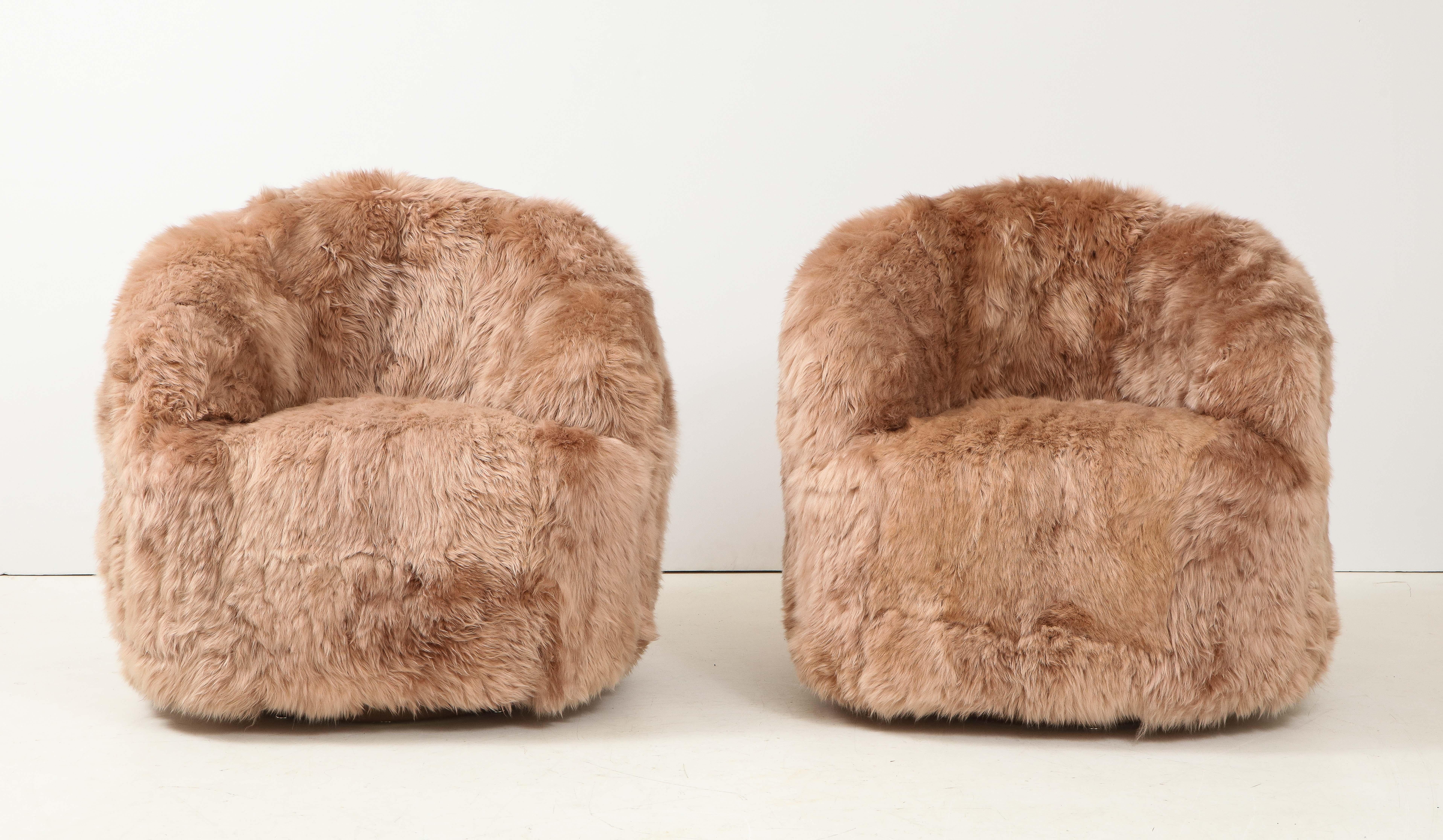 Pair of swivel club chairs custom upholstered in a sandstone / dusk colored sheepskin. Bases covered in a light brown leather. Chairs provide ample seating and are extremely comfortable. New Padding and upholstery.