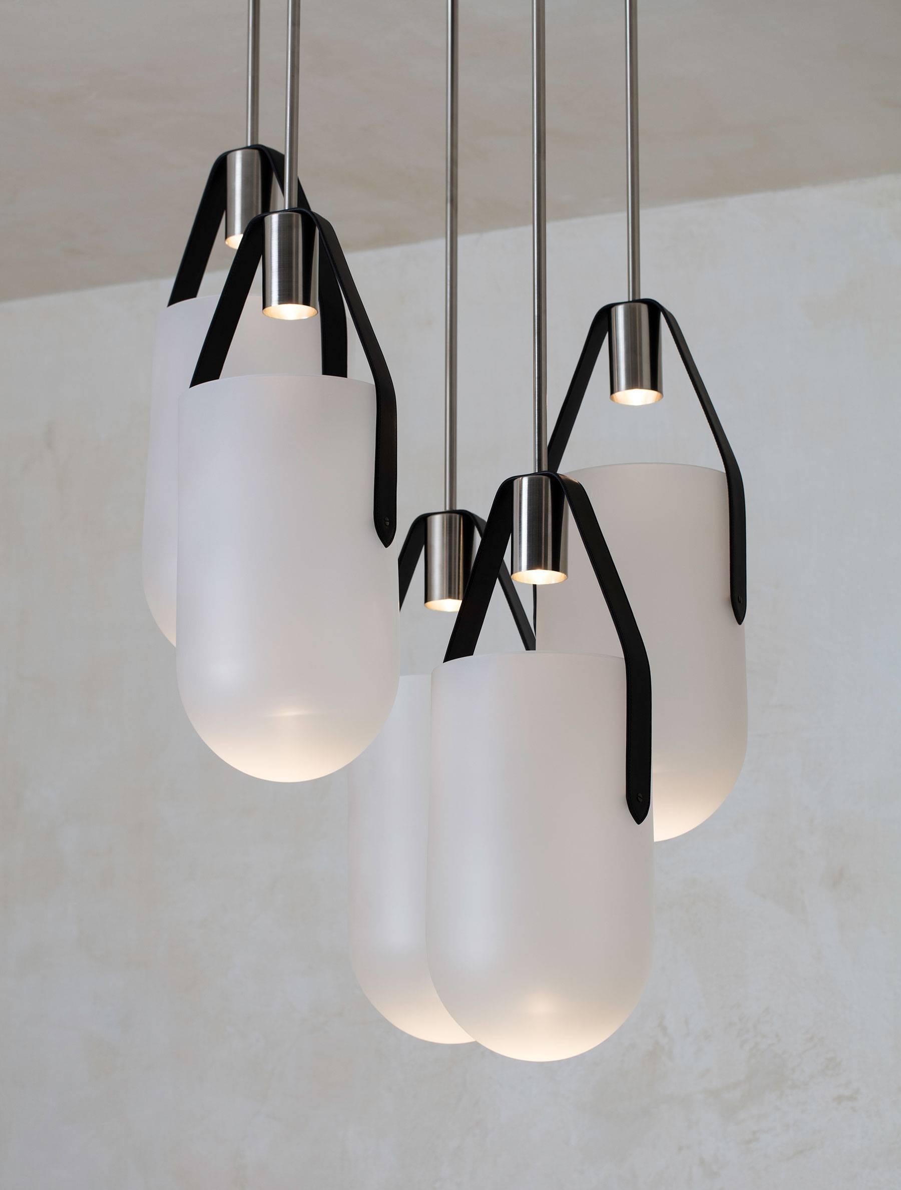 5 pendants are clustered together in an arrangement of Allied Maker’s well pendants. Each pendant features a narrow beam of light that is projected into a hand-blown Glass bell suspended by leather straps and brass hardware. The fixture creates a